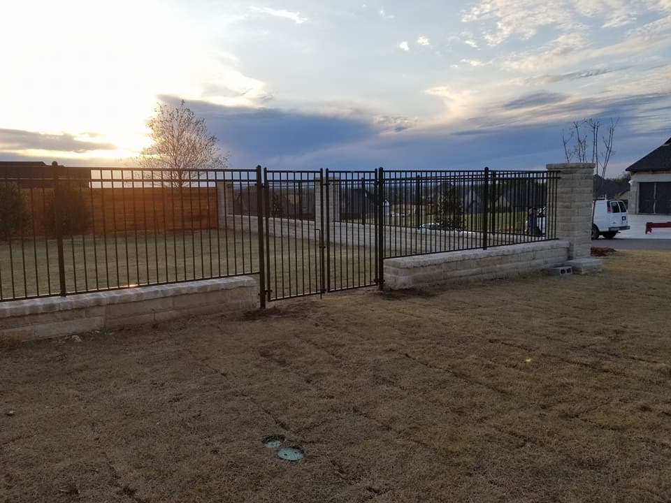 Black ornamental steel fencing with walk gate mounted on decorative stone retaining wall.