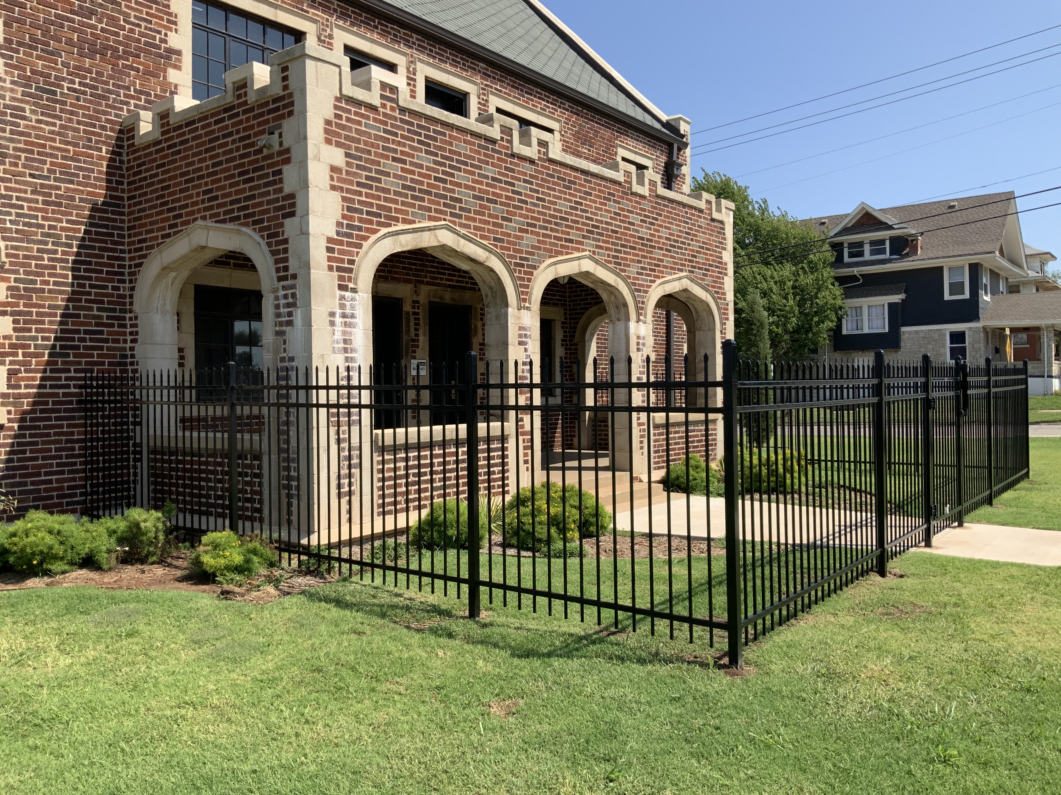 Black ornamental steel security fence installed around the brick and stone entryway of an office building.