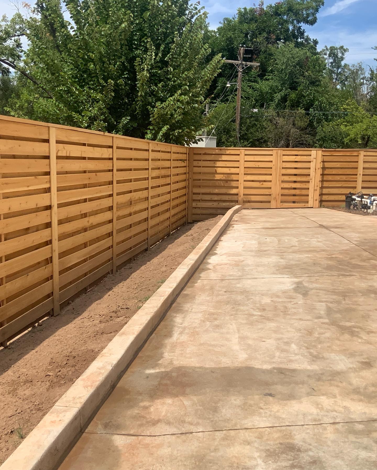 Horizontal cedar slat privacy fence with custom gate enclosure bordering concrete drive area.