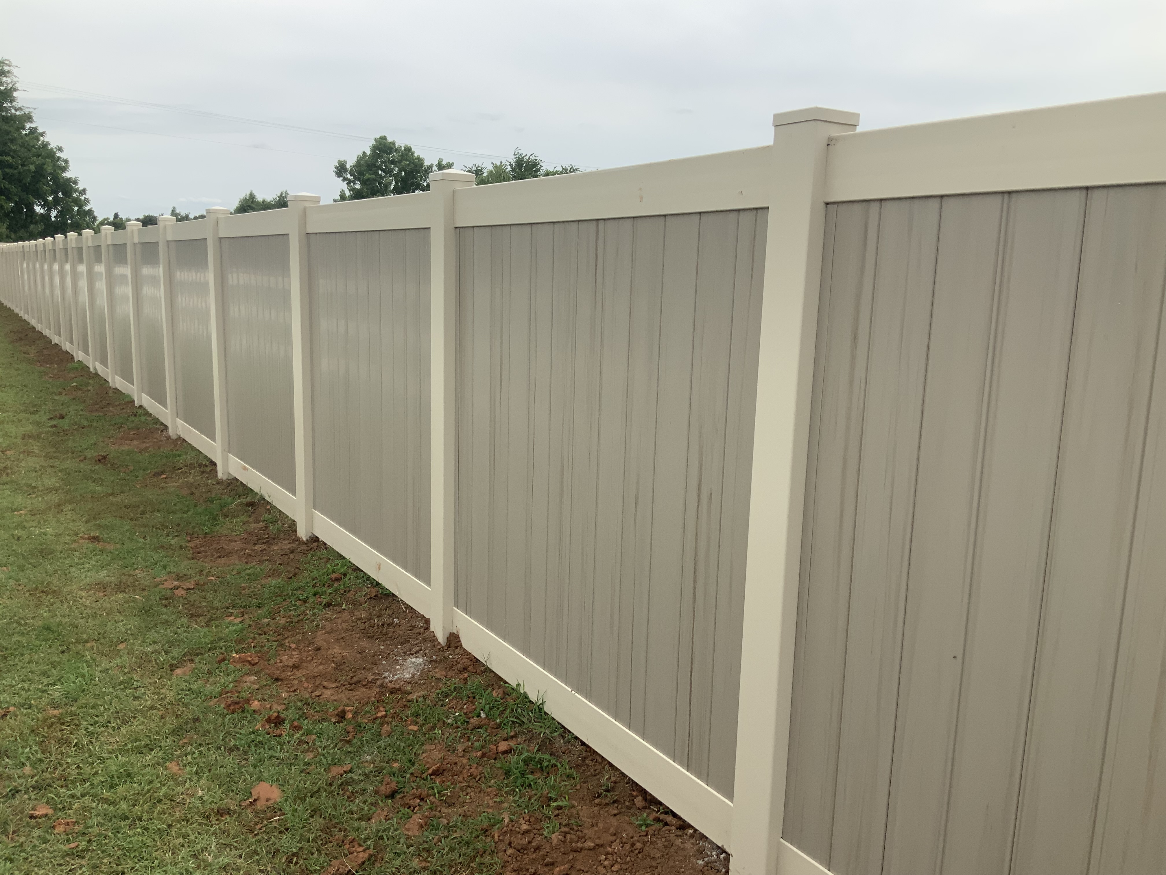 Long run of clean two-tone vinyl privacy fencing installed along property line.