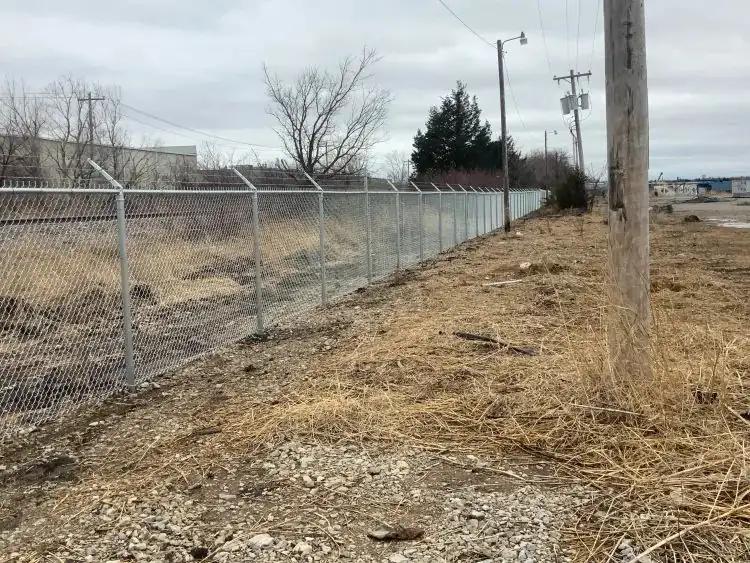 Commercial galvanized chain link security fence topped with barbed wire running along an industrial boundary.