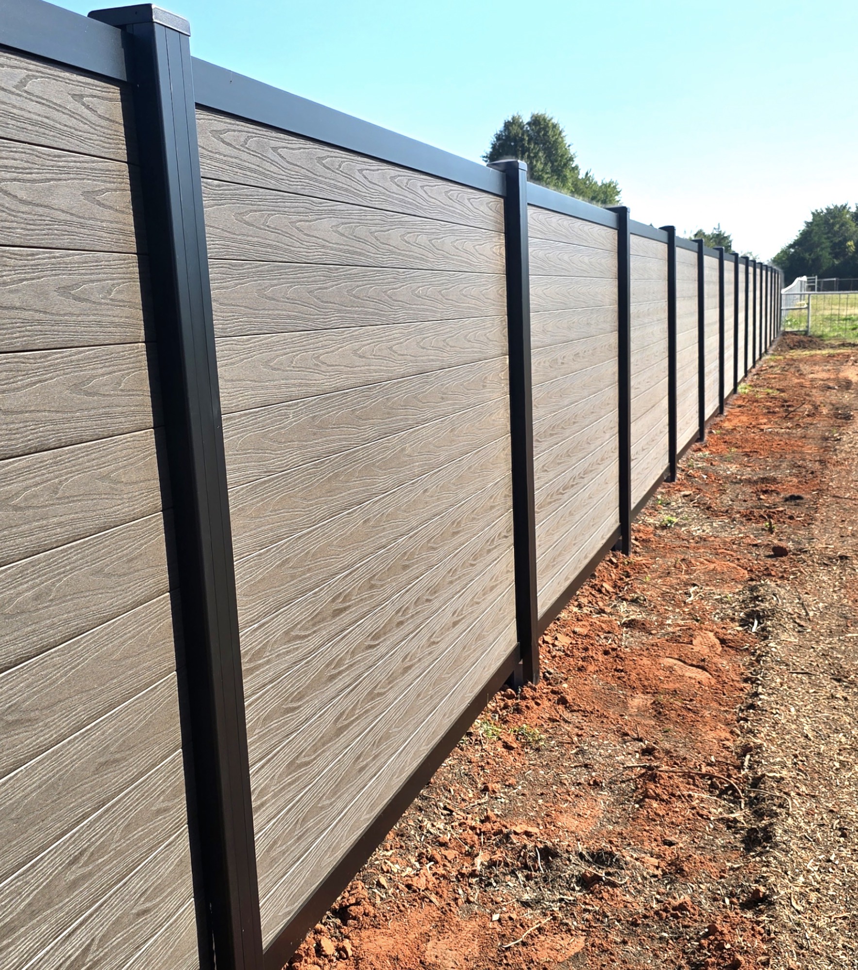 Close-up perspective of durable textured wood-grain composite fence panels and black posts.