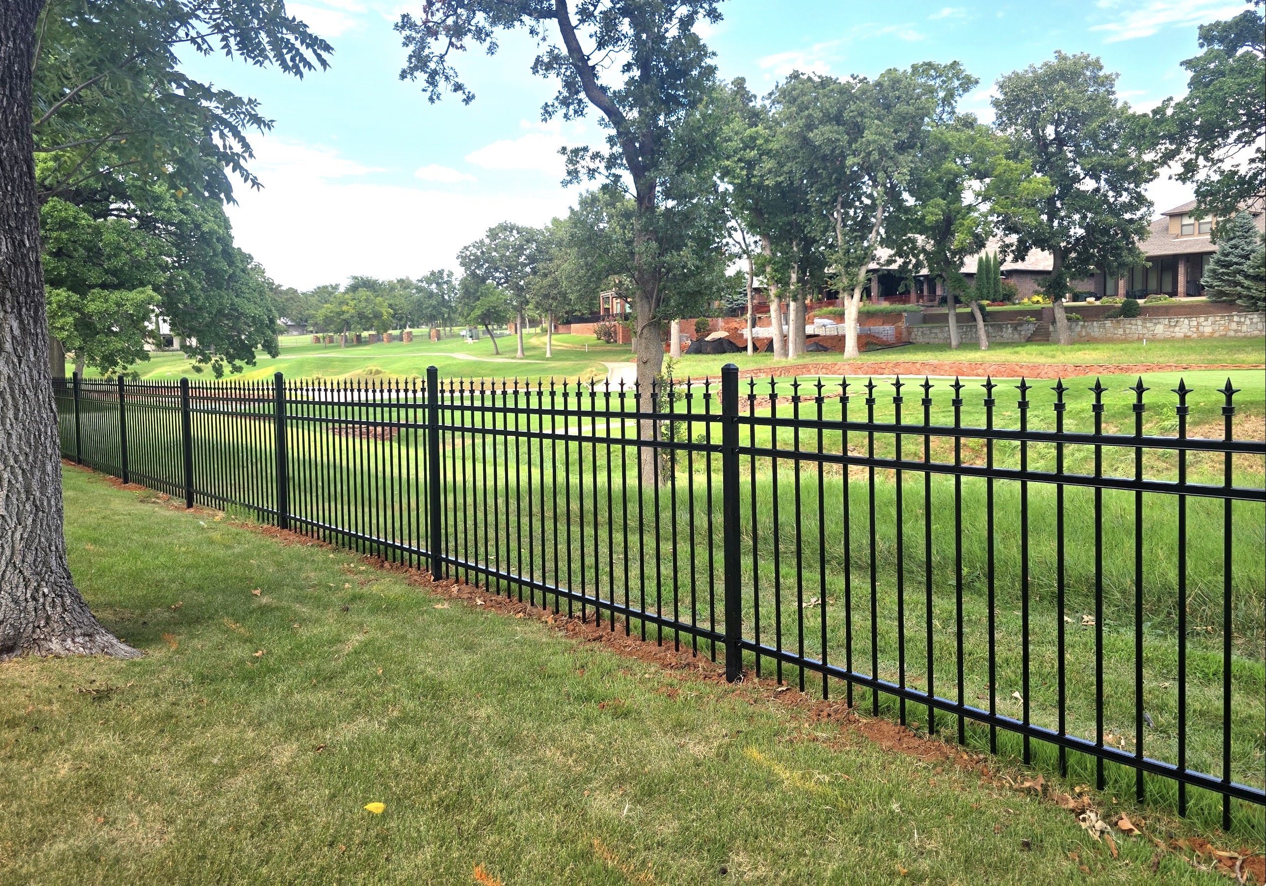 Black ornamental steel fence with decorative triad spear finials installed along lawn perimeter overlooking golf course greens.