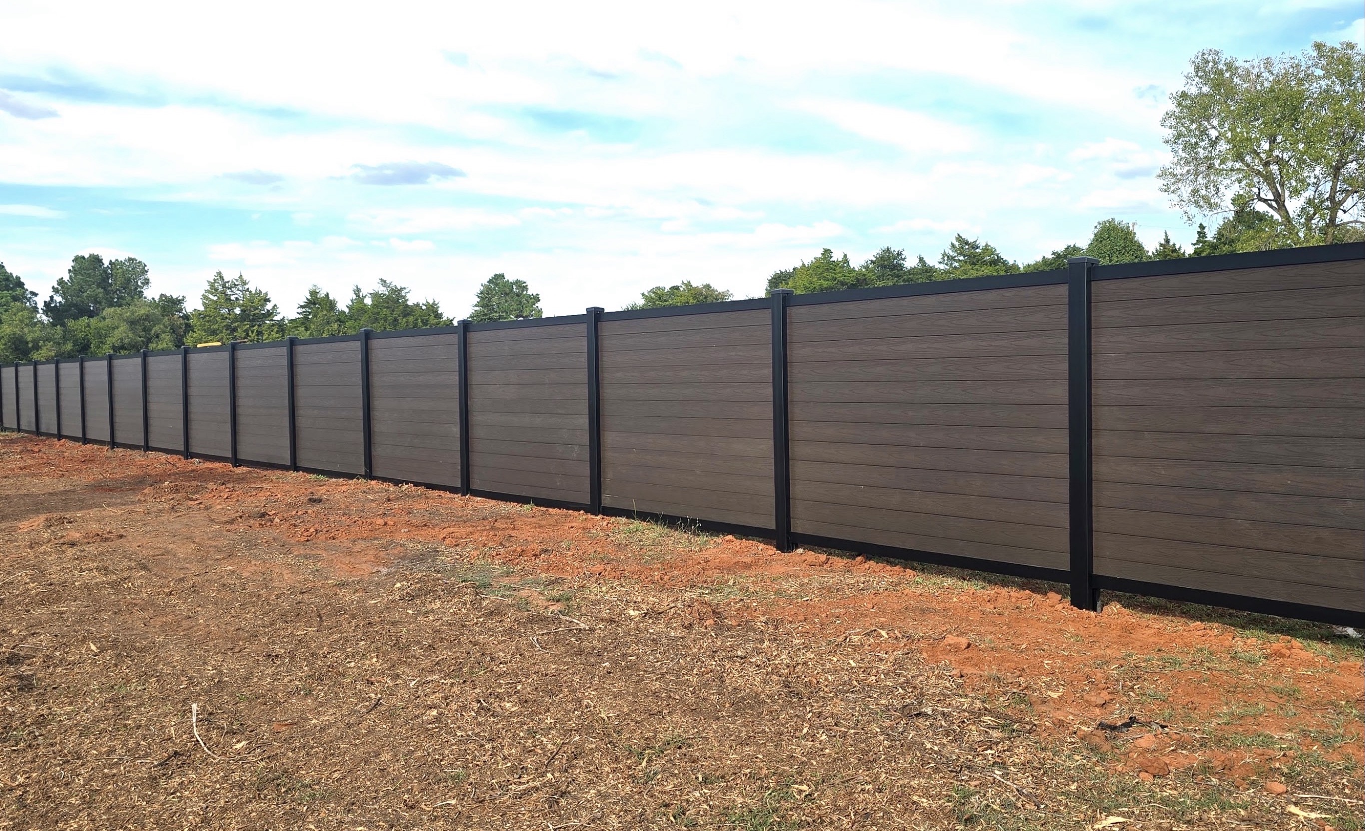 Modern horizontal wood-grain composite privacy fence with black posts and top rail against open sky.