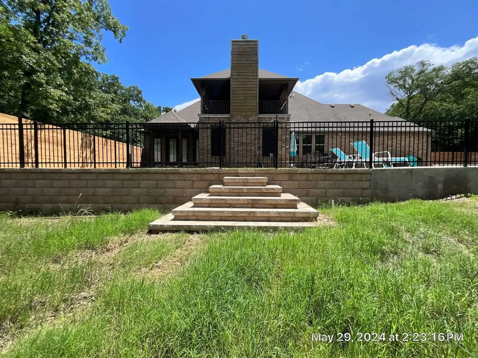 Black ornamental steel pool fence mounted along a stone retaining wall with center steps.