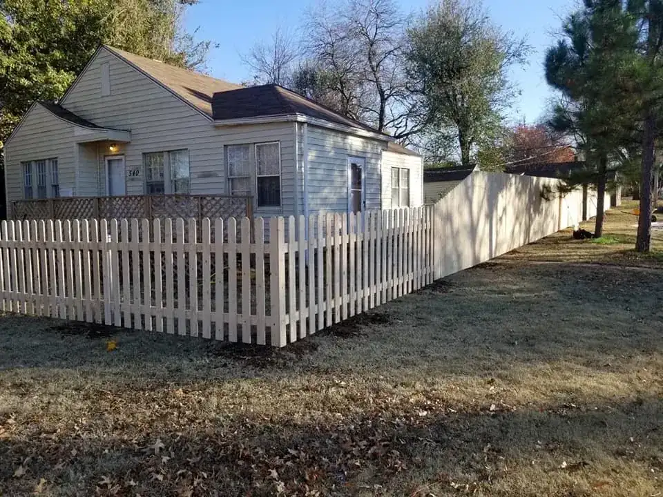 Spaced cedar picket fence enclosing front yard and stepping up into tall wood privacy fence along property line.