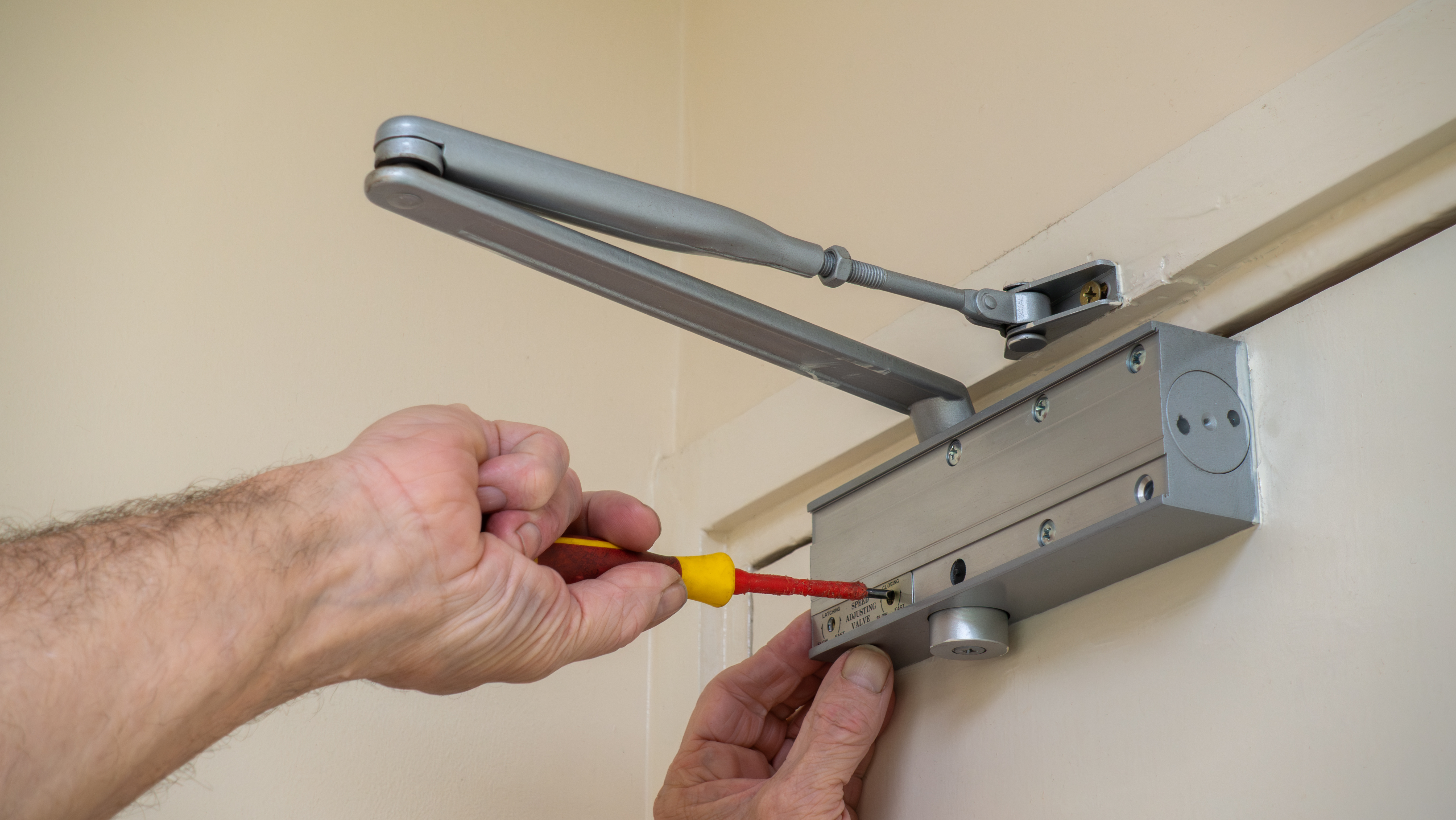 Hands adjusting an overhead fire door closer mechanism with a screwdriver