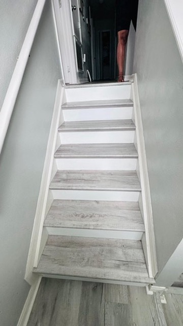 Finished enclosed staircase with light gray wood plank treads and white risers matching baseboards and stringers