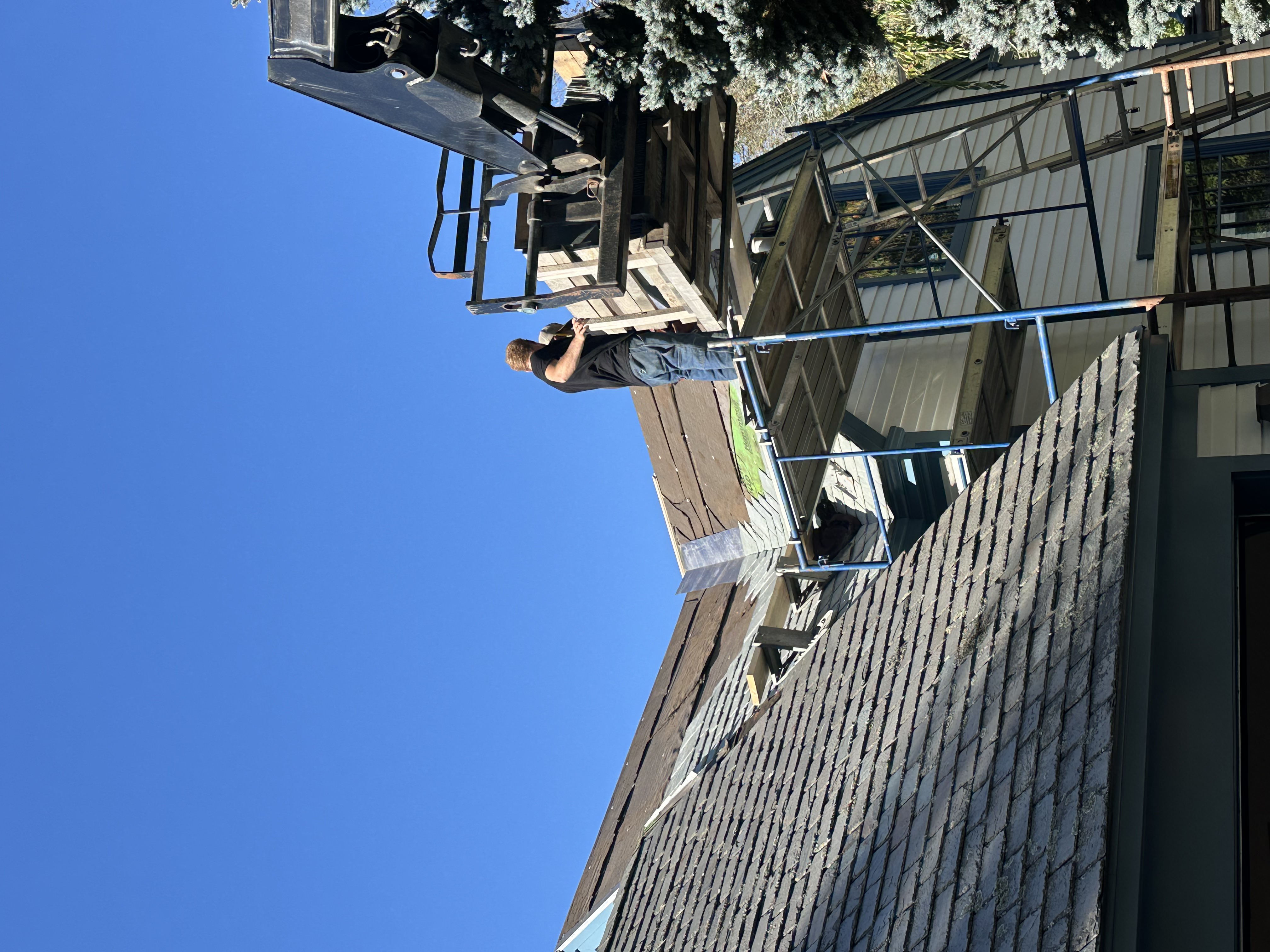 Crane delivering slate materials to roof with scaffolding on Vermont home