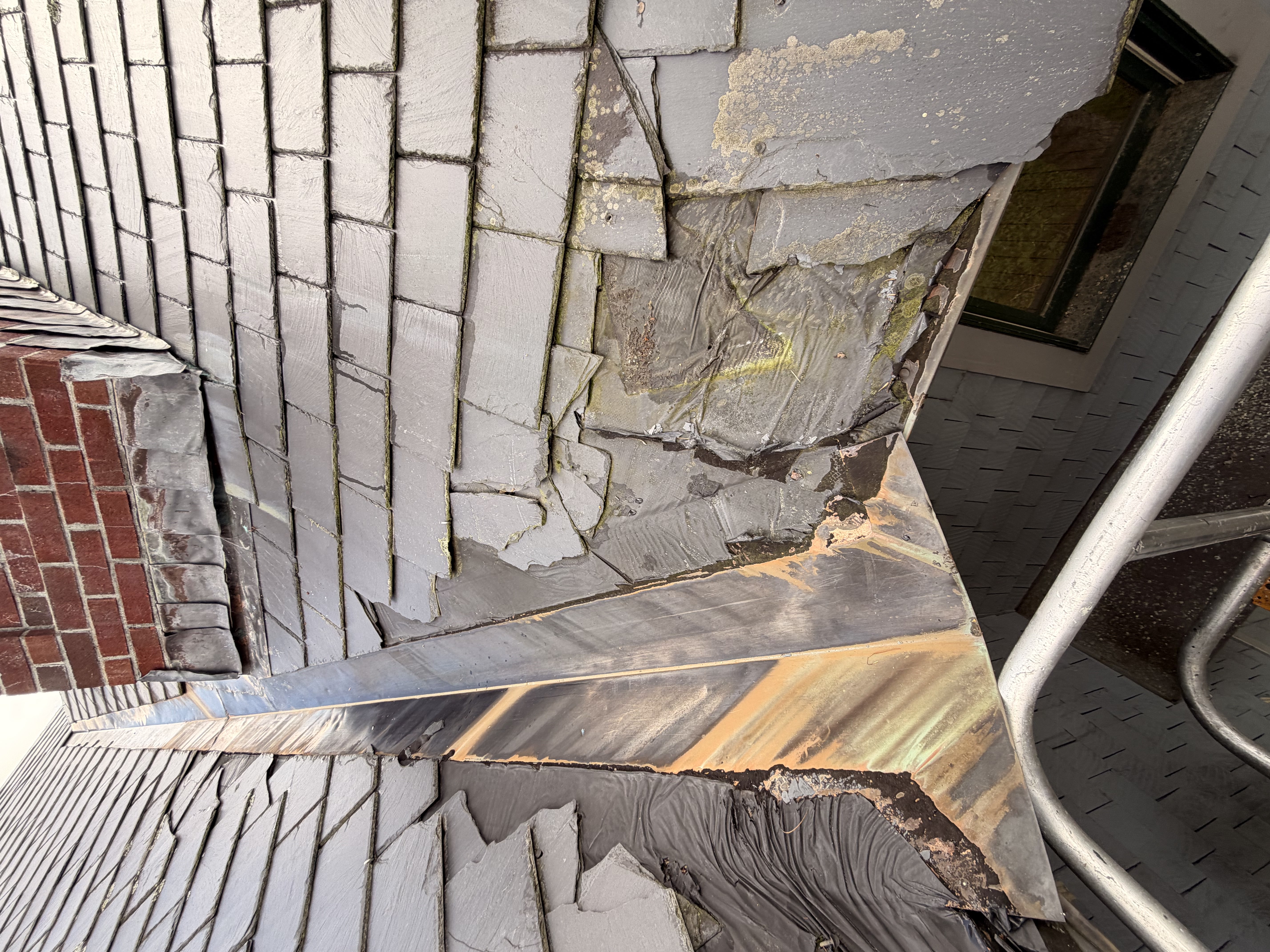 Moss-covered slate roof with slipped tiles and failing underlayment on brick home