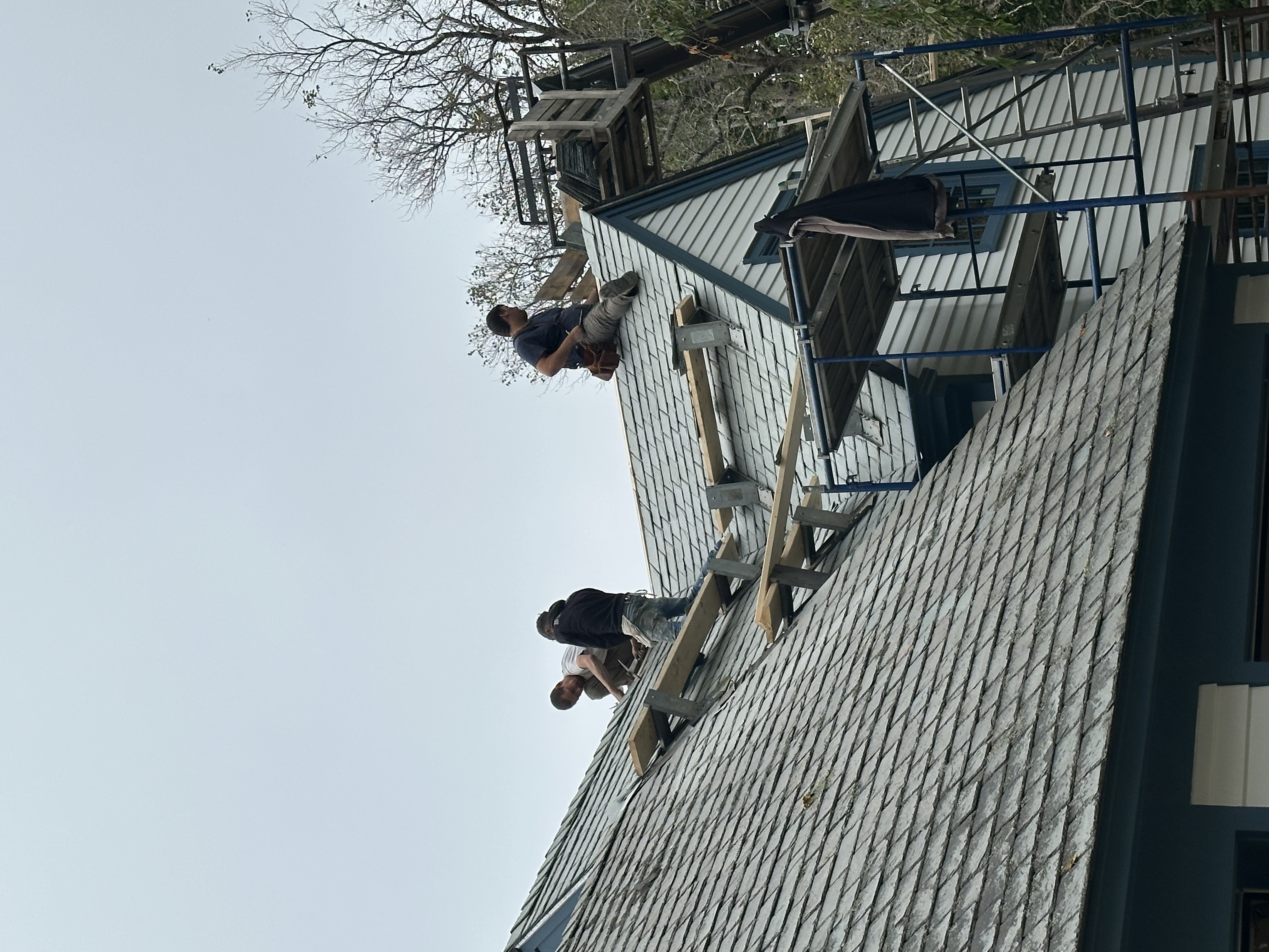 Multiple crew members collaborating on steep slate roof installation project