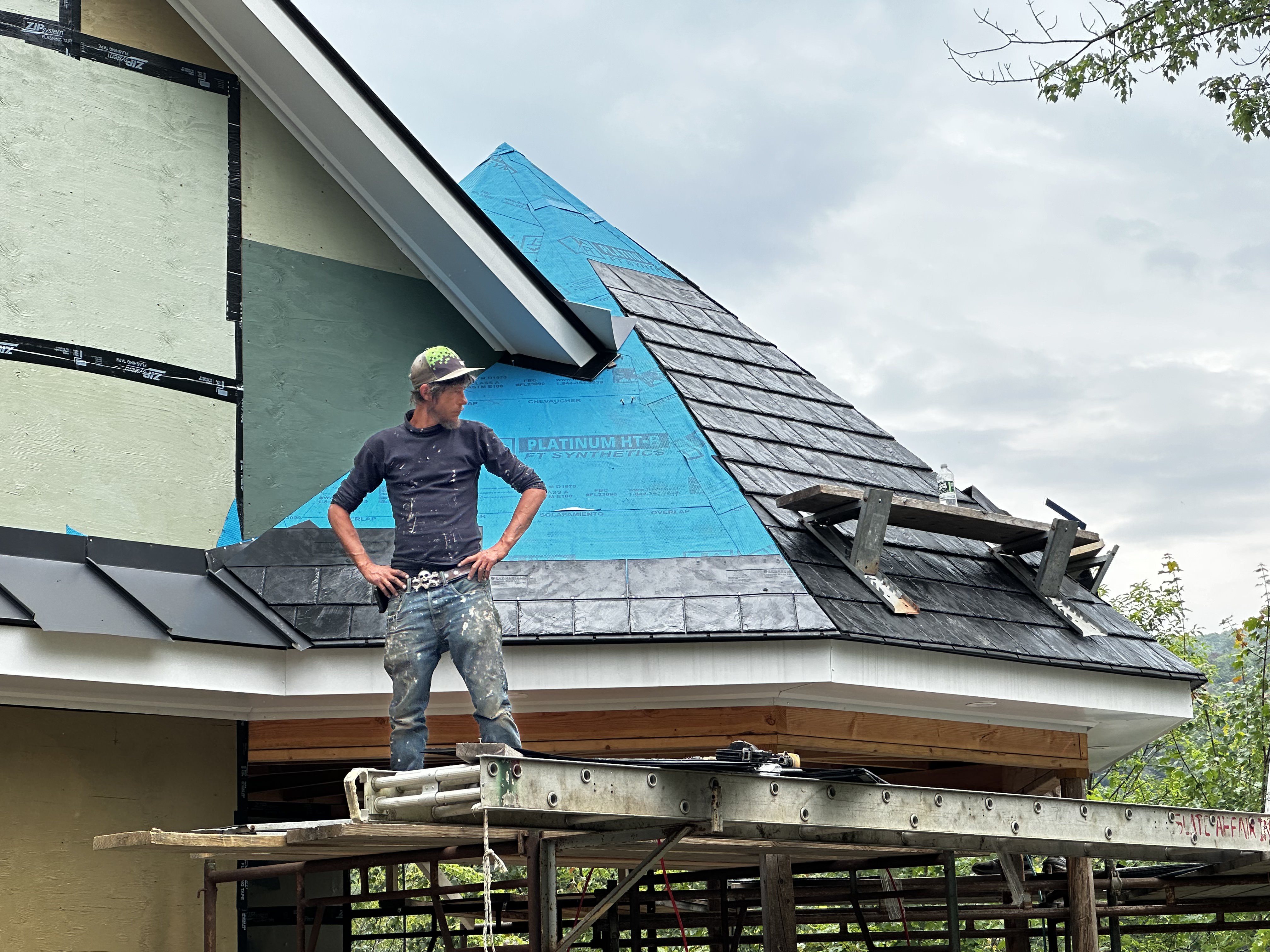 Roofer on scaffolding during slate tile installation with protective underlayment visible