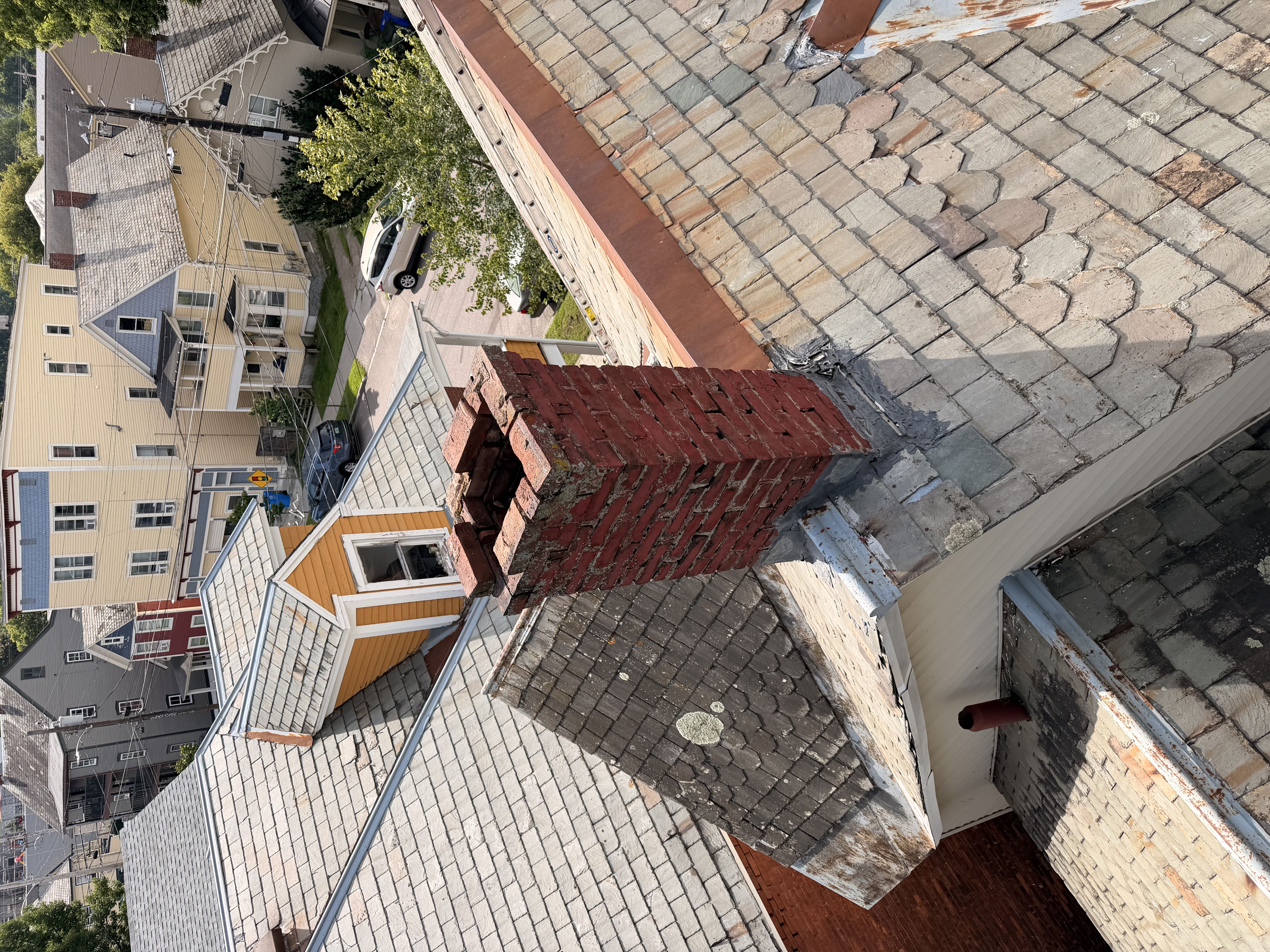 Aerial view of multi-colored natural slate roof with brick chimney in historic neighborhood