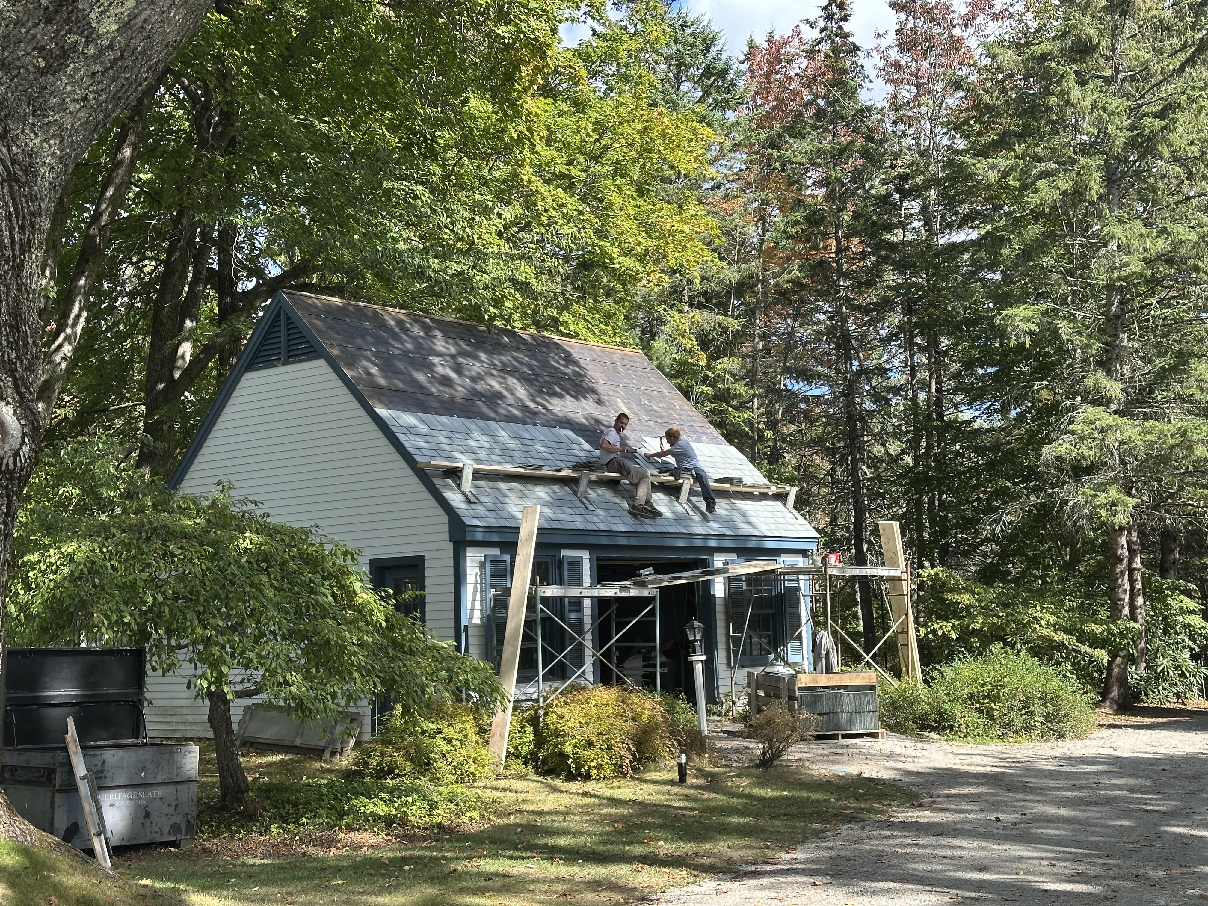 Team working on slate roof installation of white home with blue trim windows
