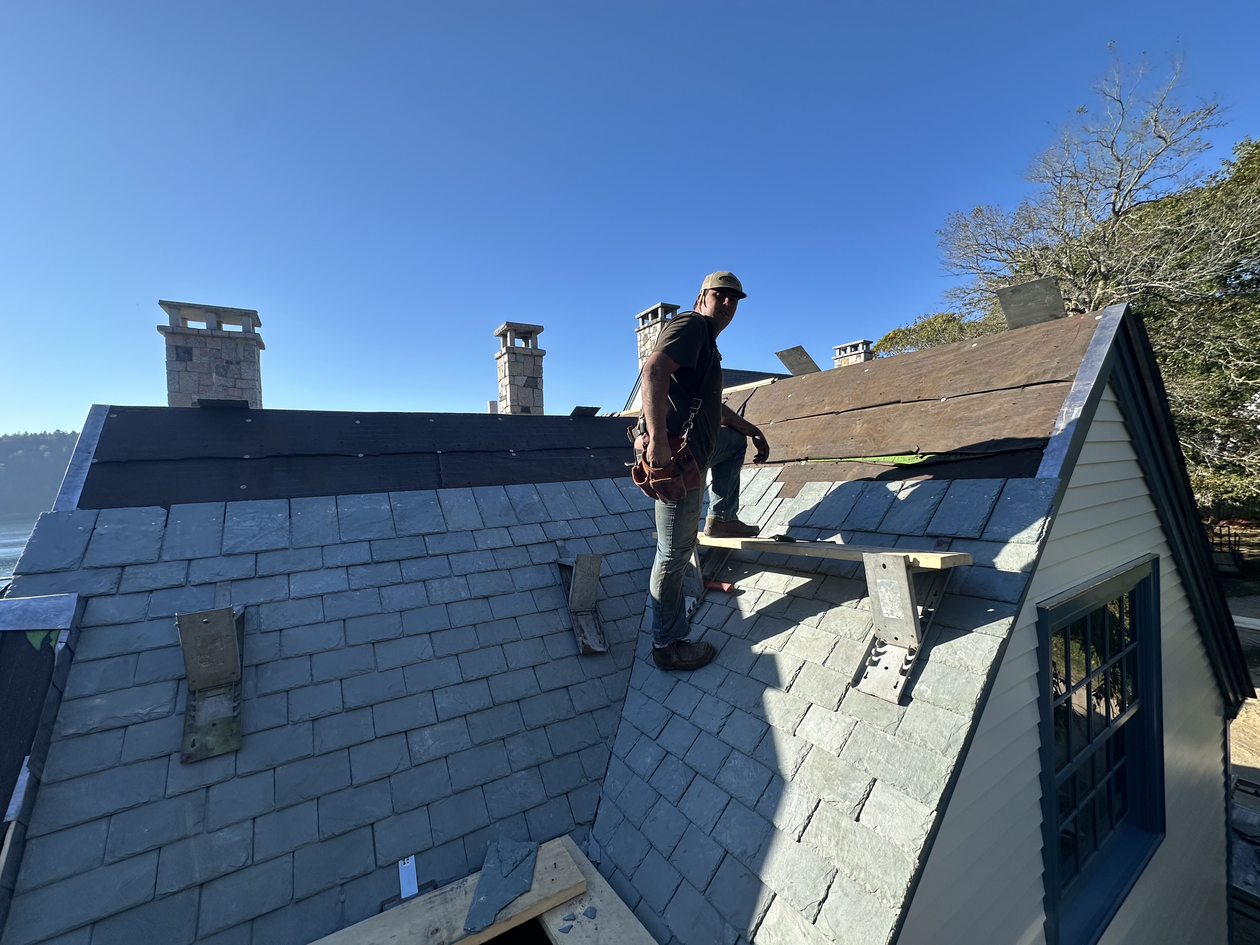 Experienced roofer standing on newly installed gray slate roof with tool belt
