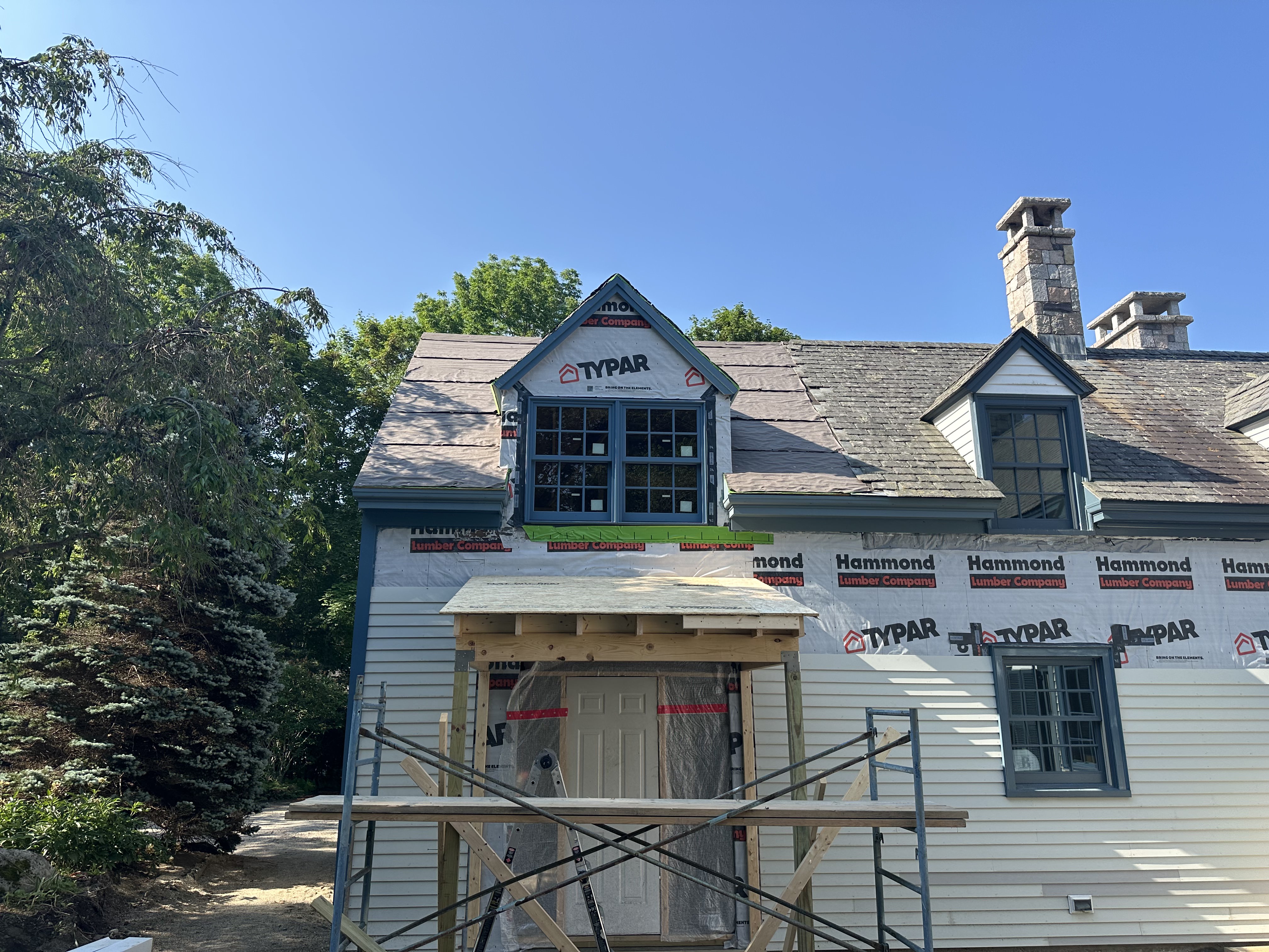 Colonial style home with slate roofing under construction and stone chimneys