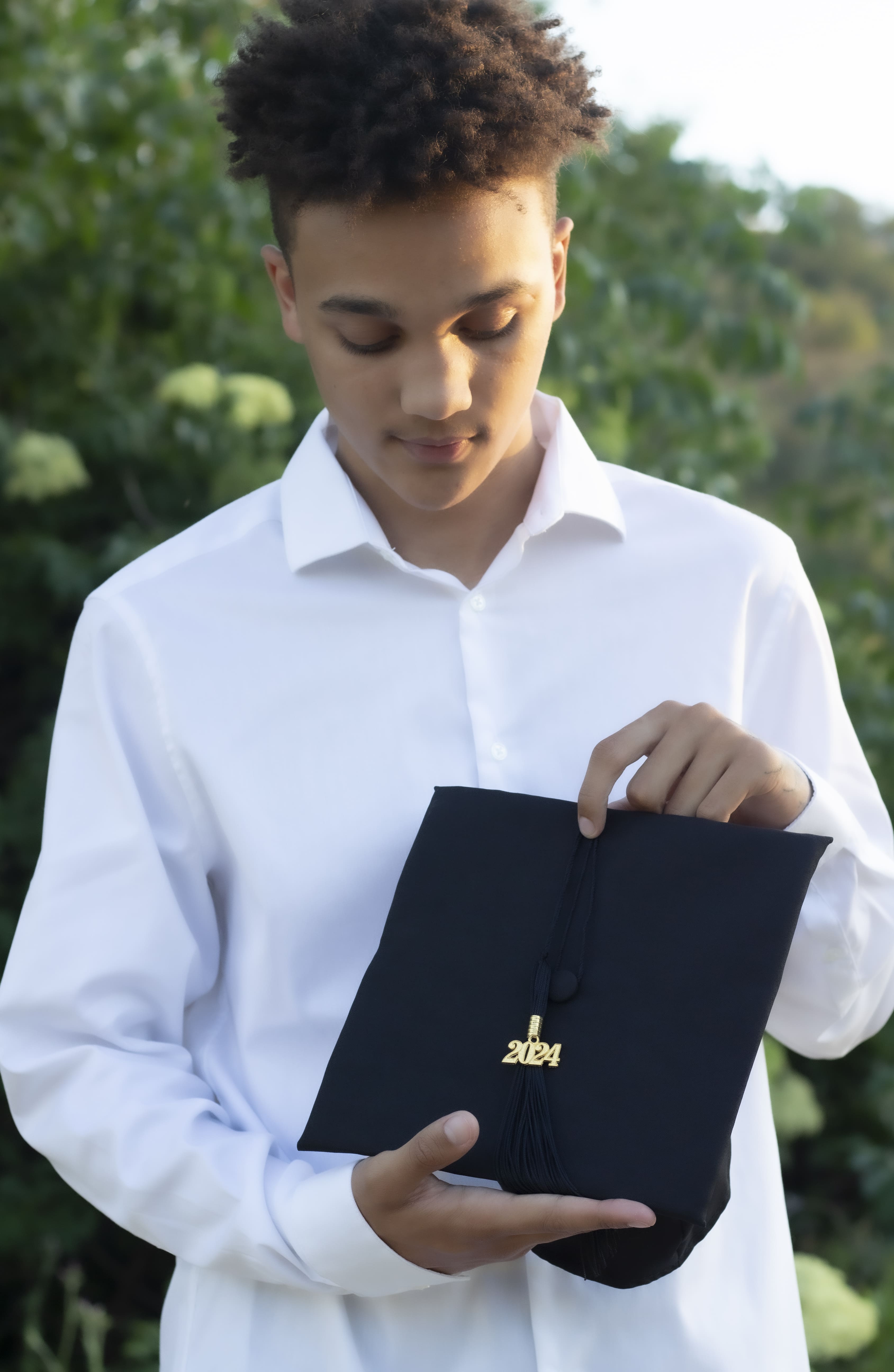 Senior in white shirt holding 2024 graduation cap by Brooke Lazzarini