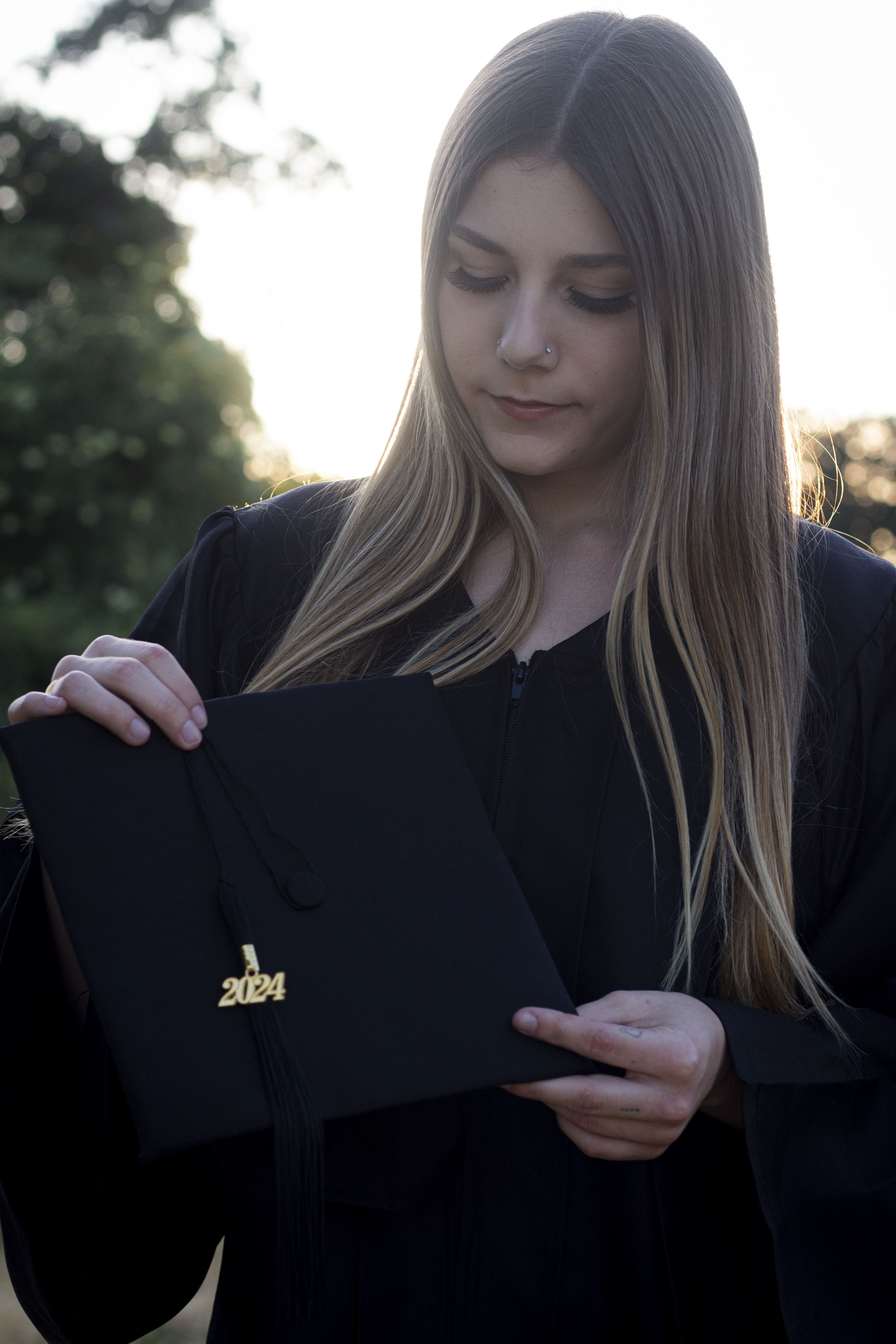 Senior in graduation gown holding 2024 diploma by Brooke Lazzarini