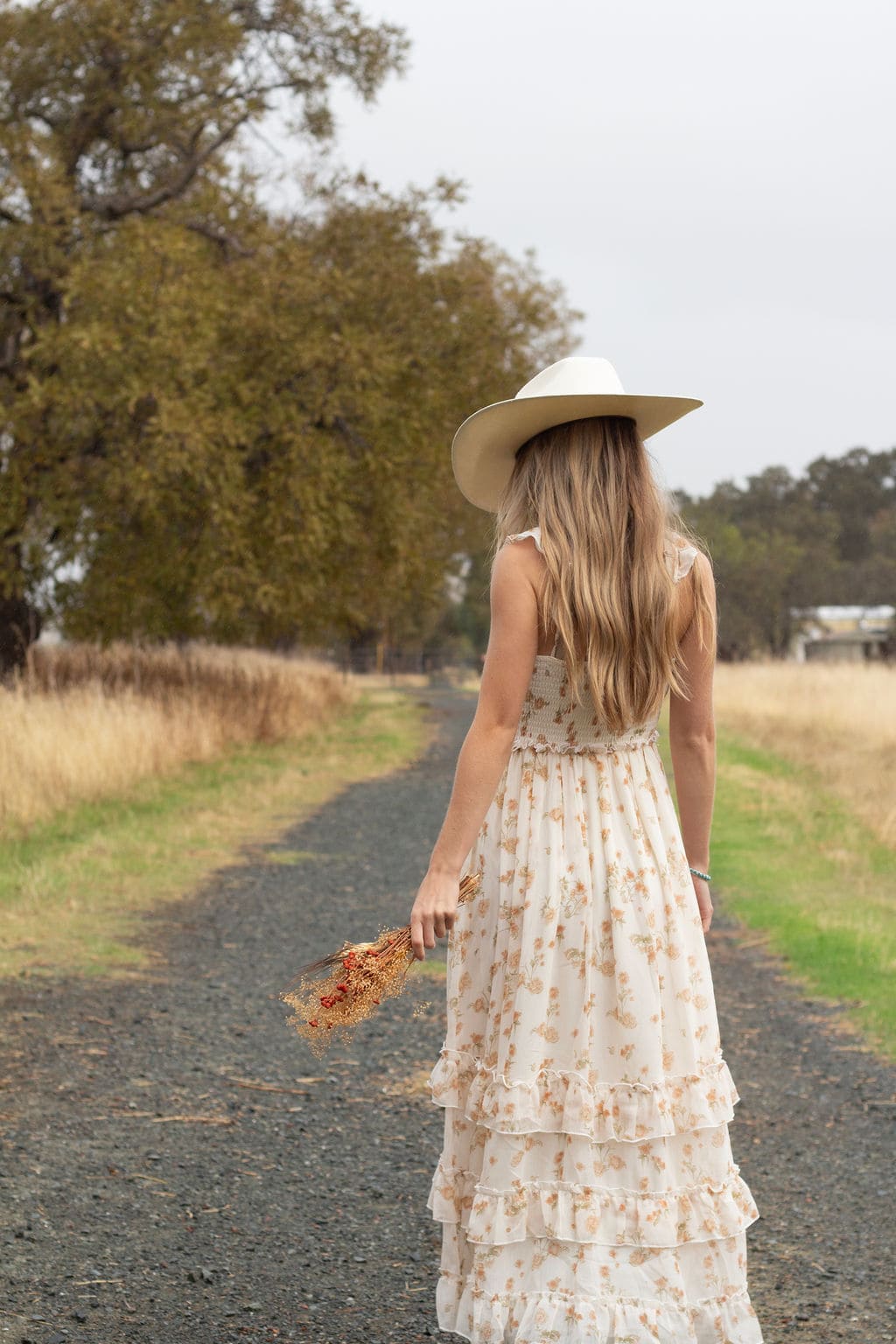 Cowgirl in floral dress walking down country road by Brooke Lazzarini