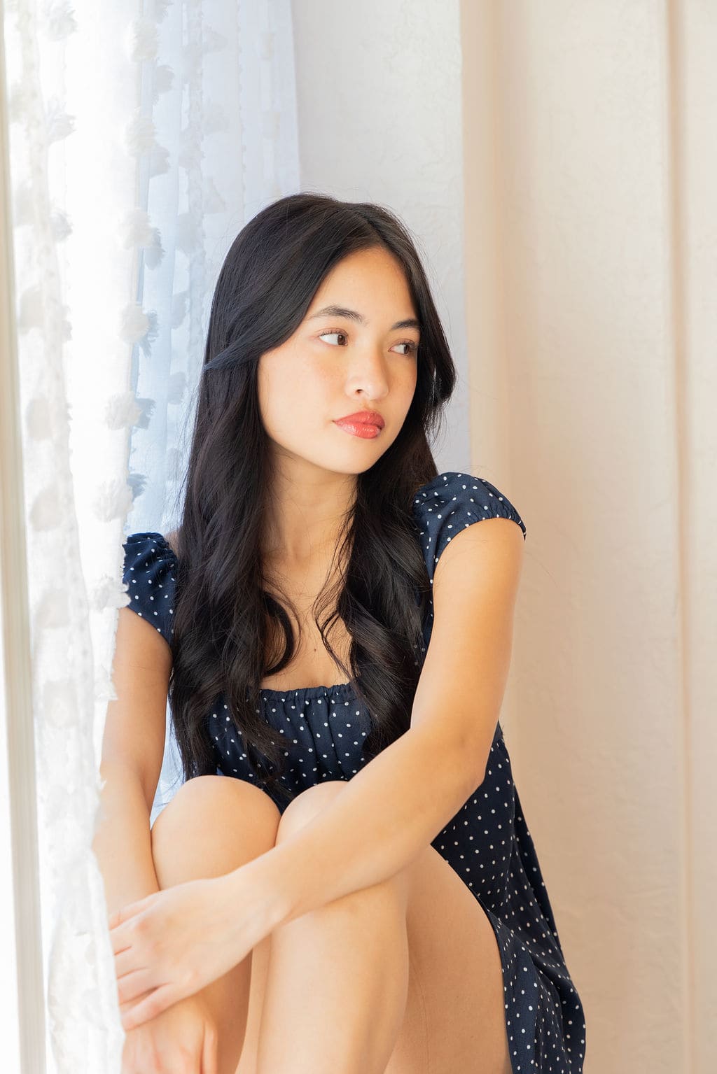 Senior in navy polka dot dress seated by window by Brooke Lazzarini