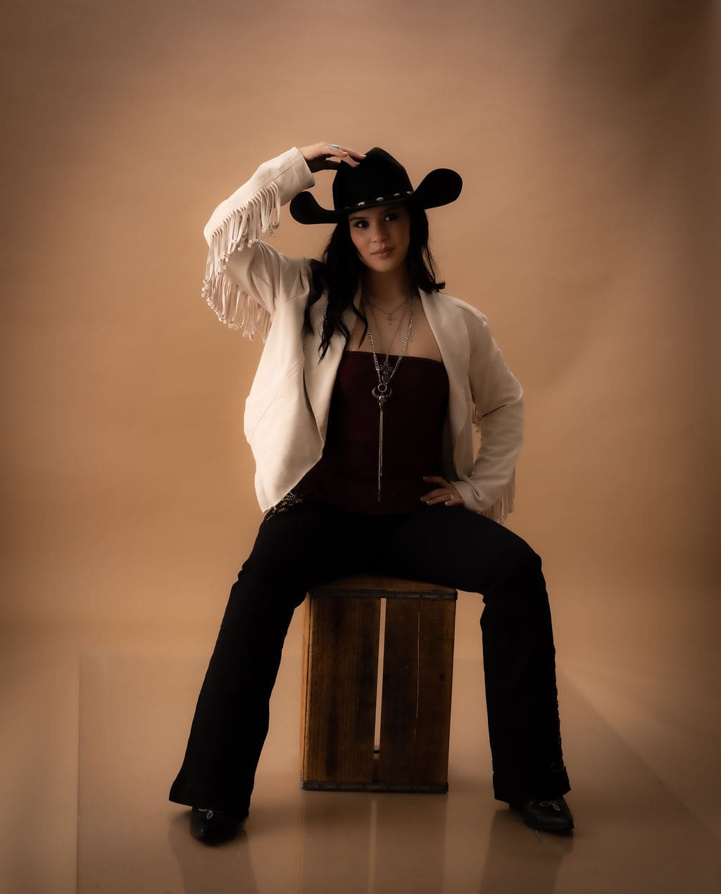 Cowgirl seated with hand on hat brim by Brooke Lazzarini