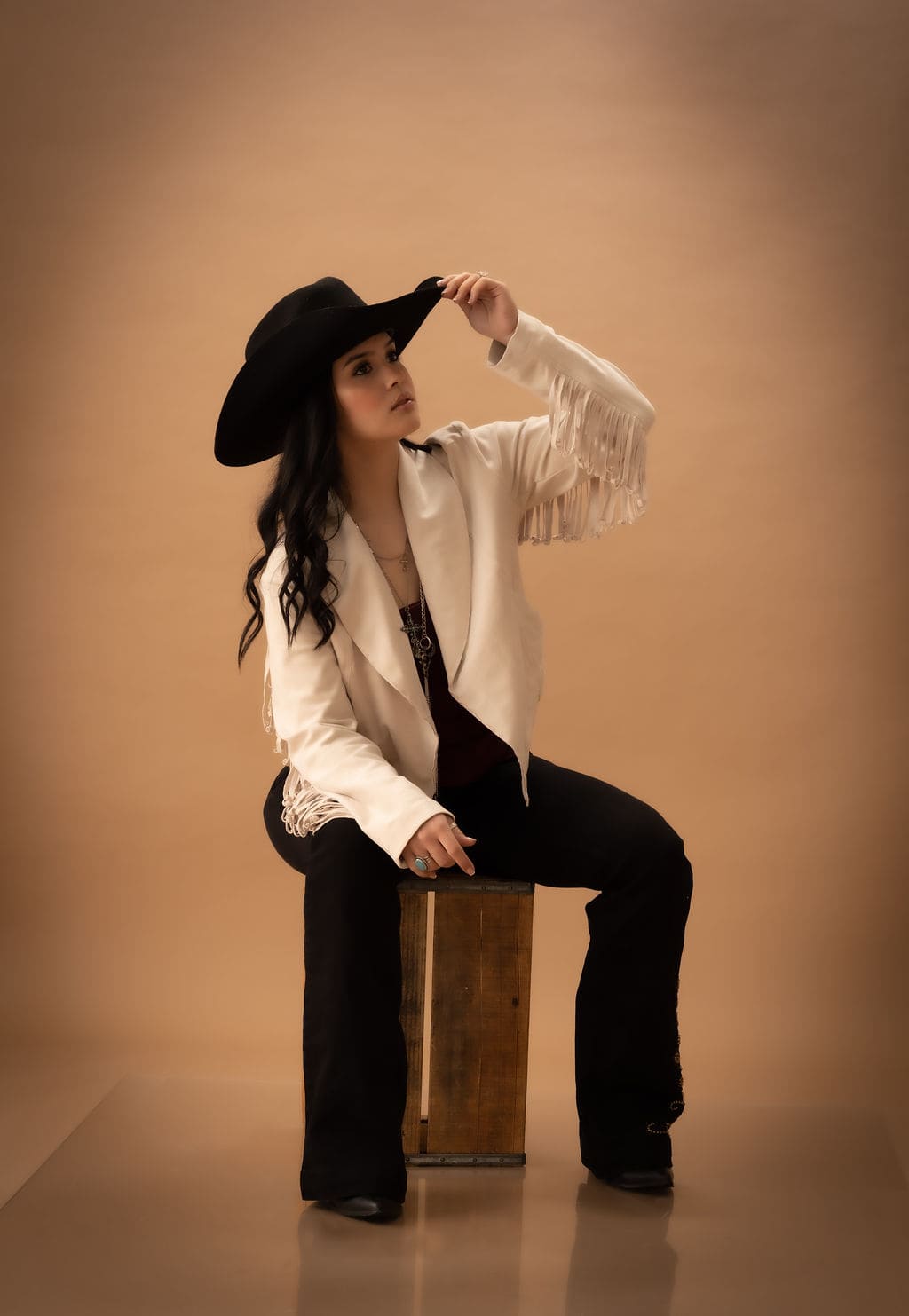 Cowgirl sitting on crate with hat by Brooke Lazzarini