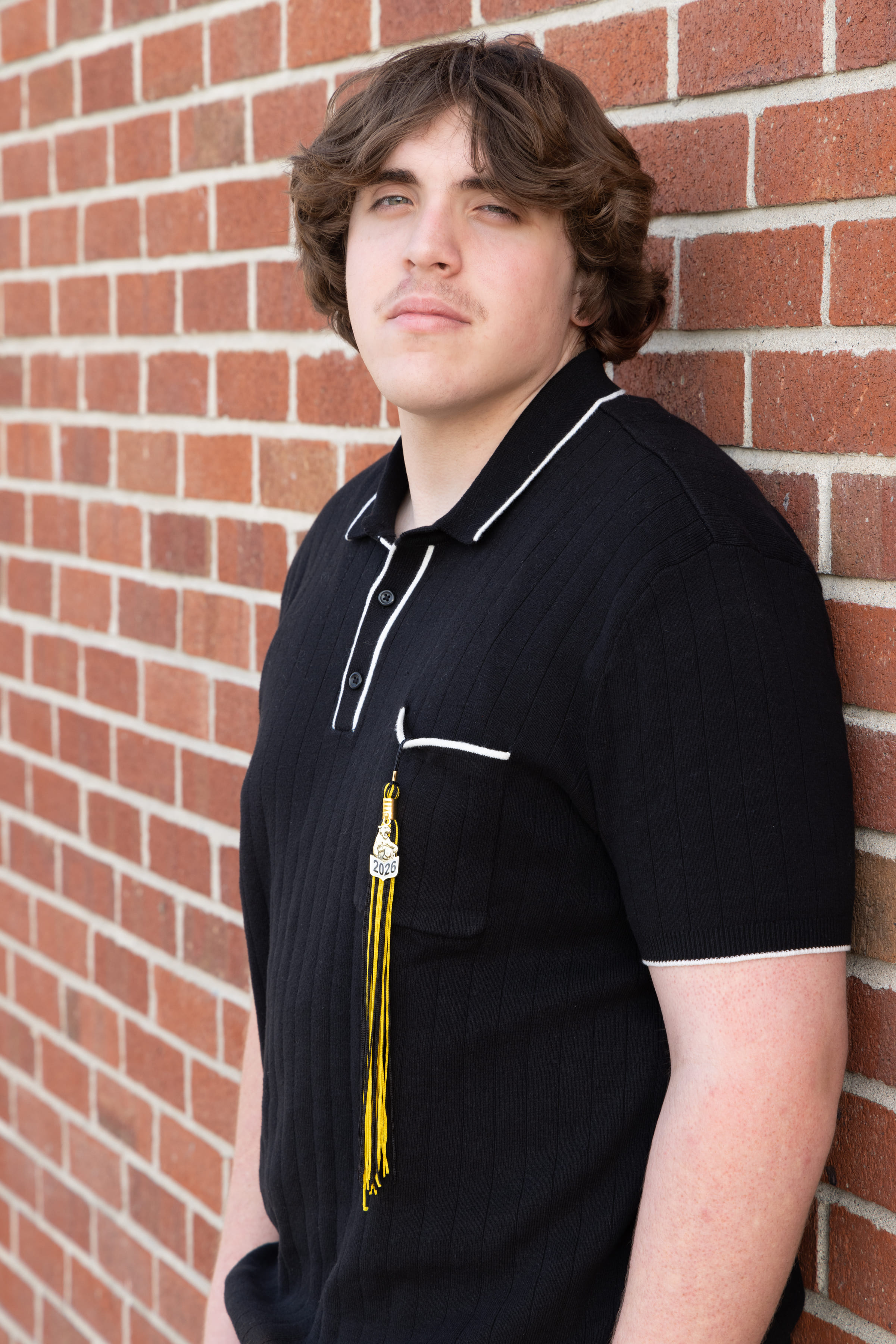 Senior in black polo with 2026 tassel against brick wall by Brooke Lazzarini