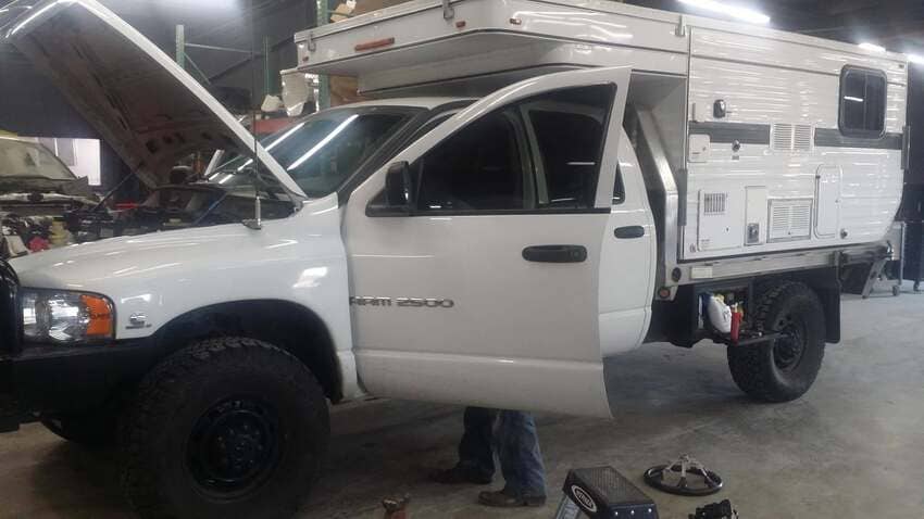 White Dodge Ram 2500 diesel truck with camper shell undergoing maintenance