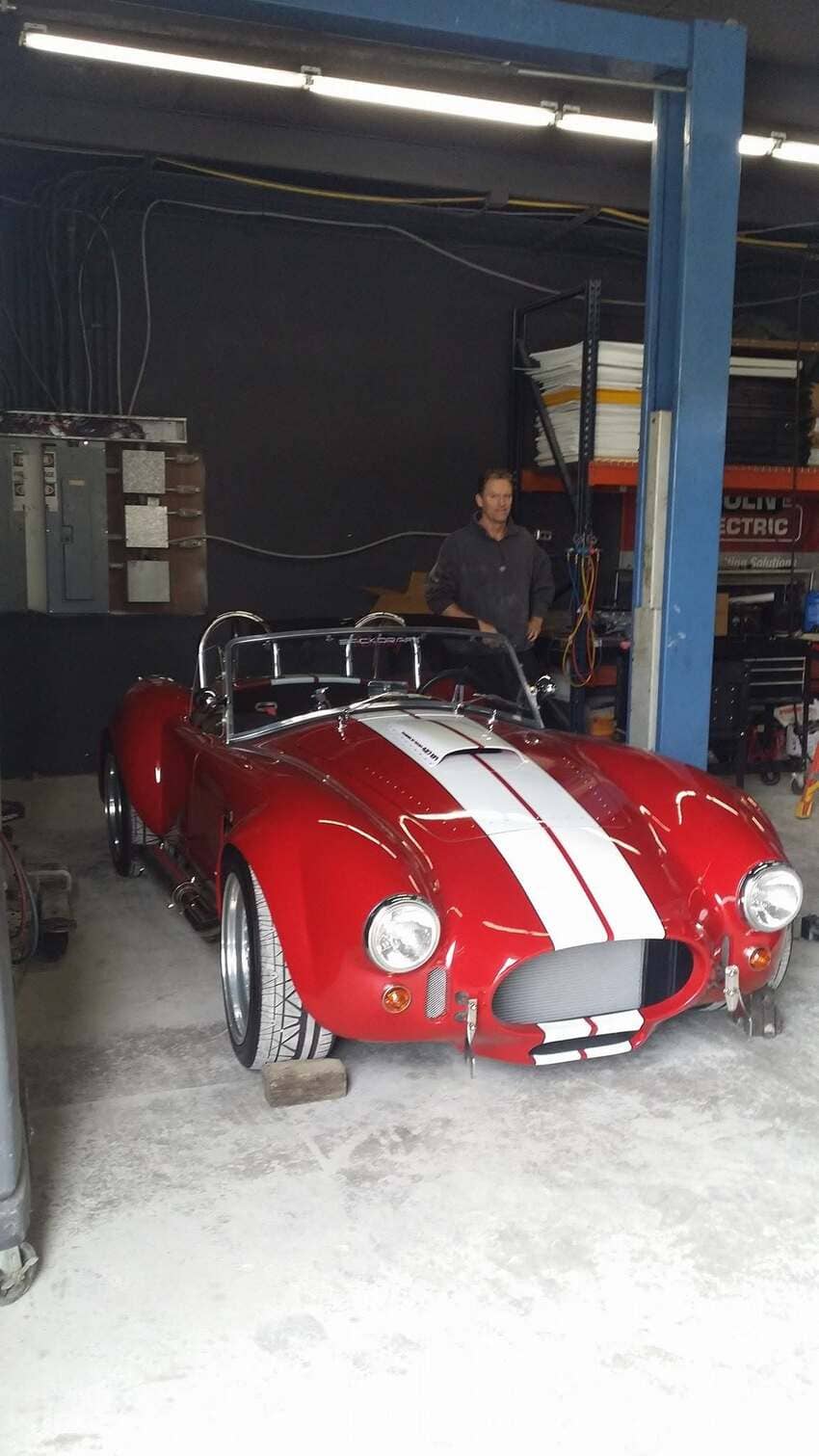 Red Shelby Cobra replica with white racing stripes in our garage showroom