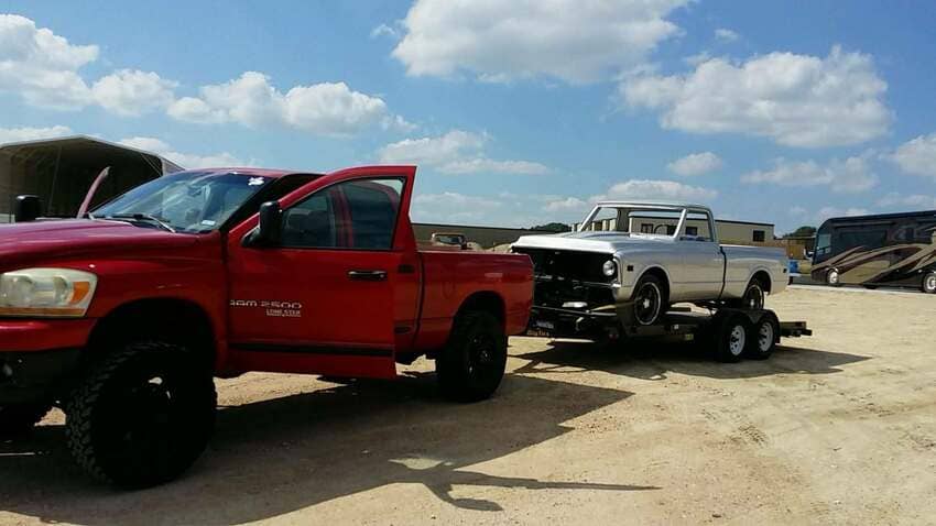 Red Dodge Ram towing classic pickup at The Austin Diesel Specialists lot