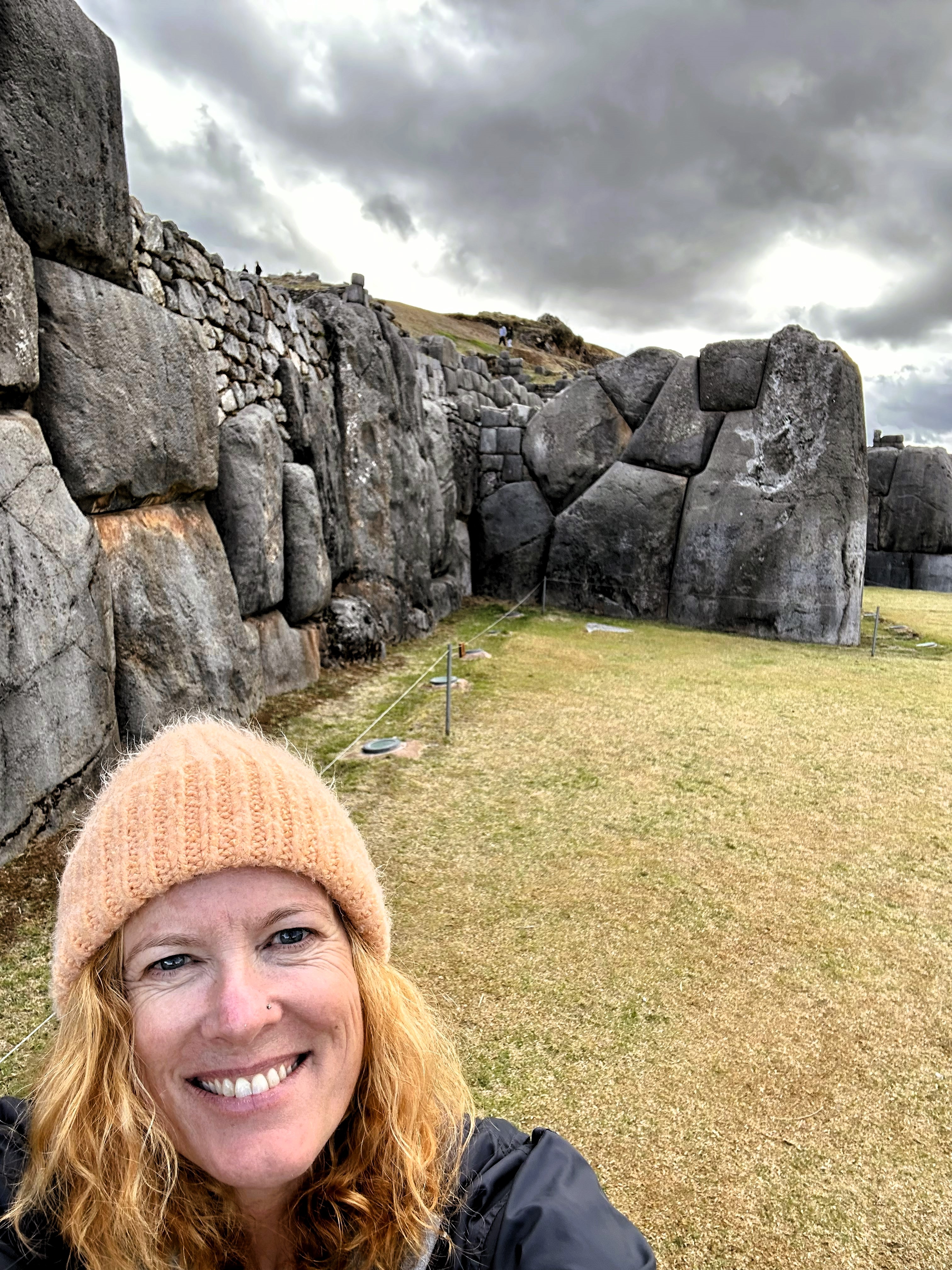 Morgan in a peach beanie smiling before ancient Incan stone walls — Peru pilgrimage, 2023