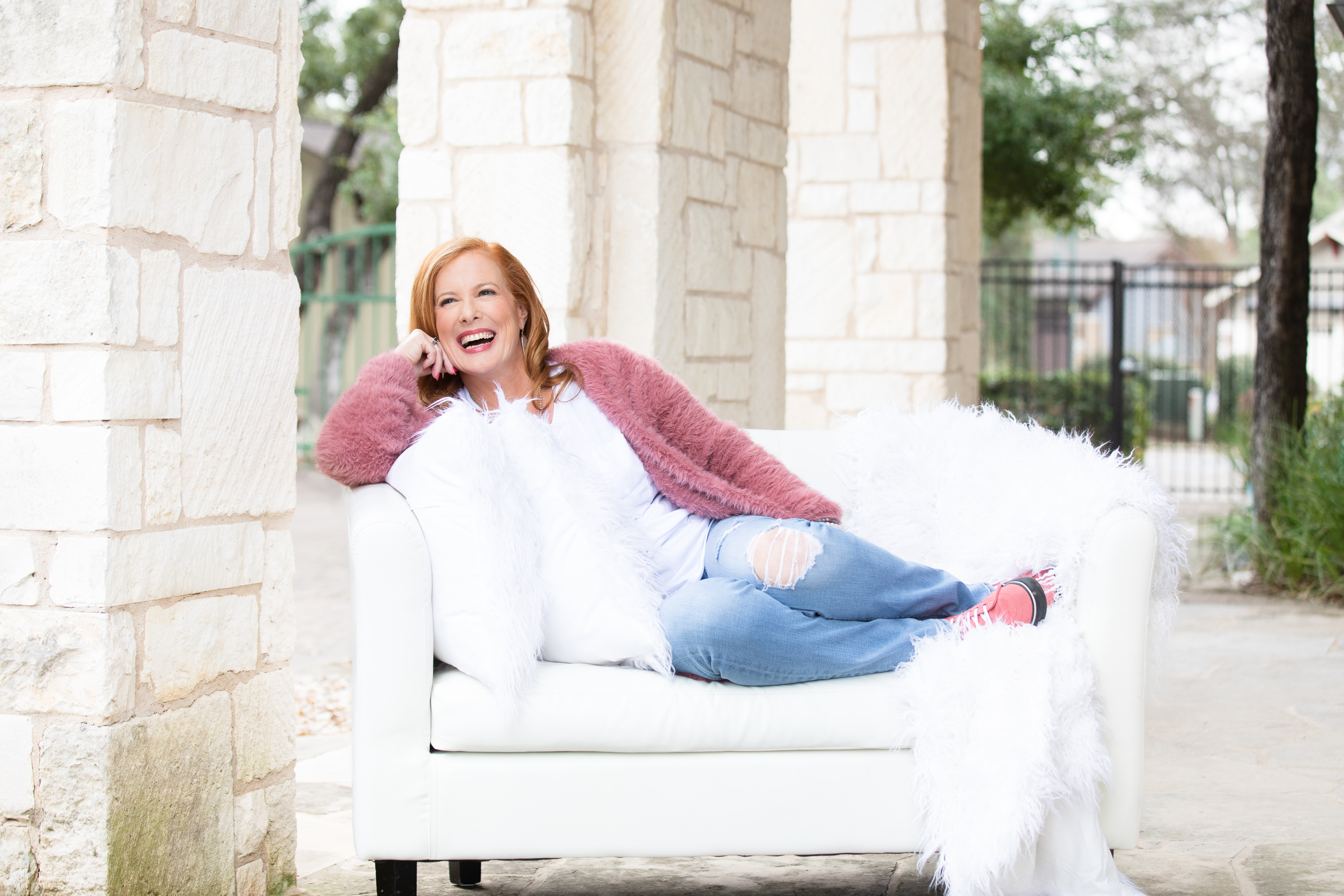 Morgan laughing on a white couch wrapped in a pink fur throw — joy, playfulness, sacred doesn't have to be solemn