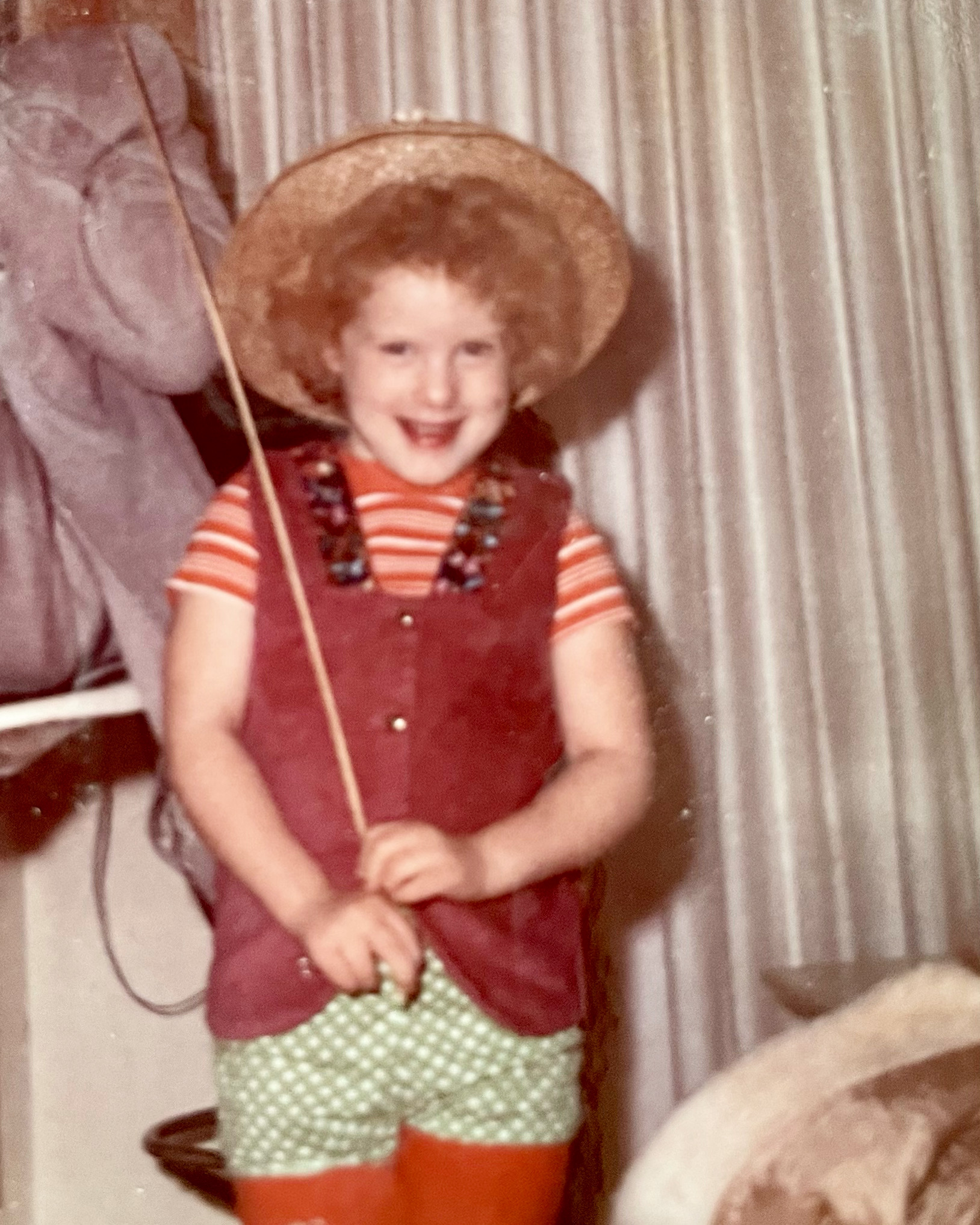 Young Morgan as a 3 year old in a straw hat and red vest, holding a stick with a joyful smile — finding her way back to herself