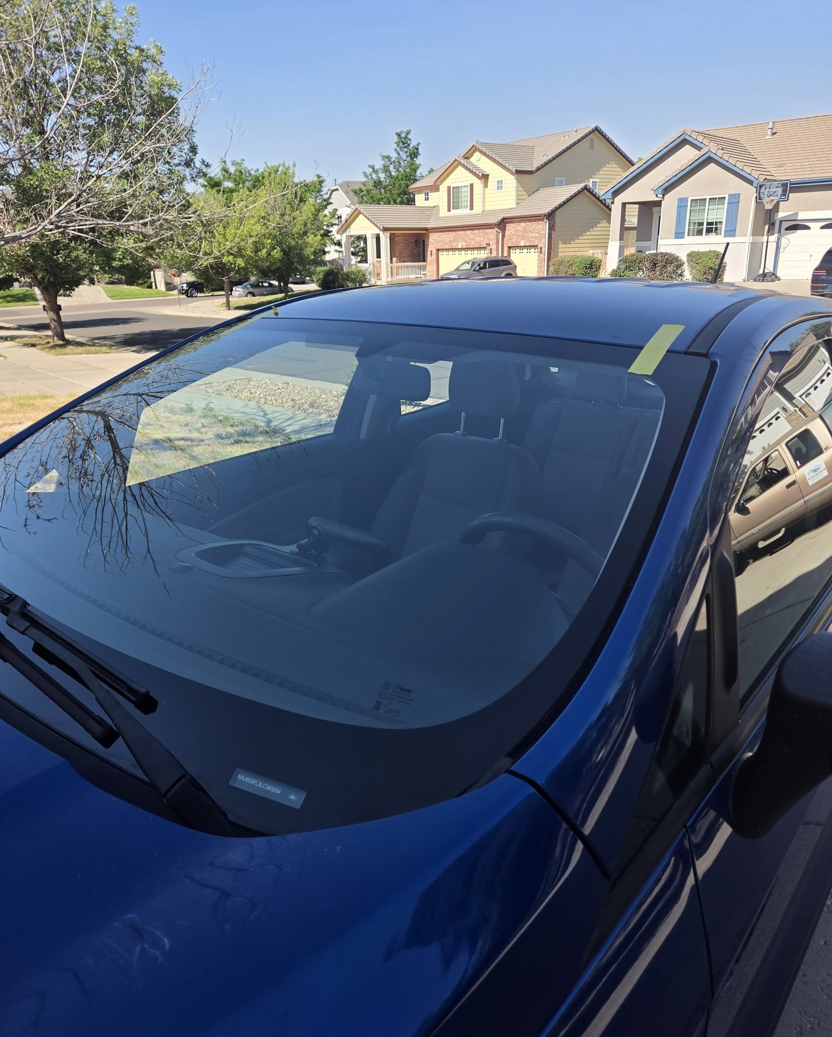 New windshield installed on blue sedan in residential driveway