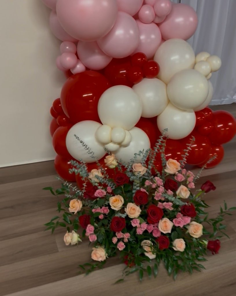 Stunning red, pink, and ivory balloon garland arrangement with fresh rose bouquet at base