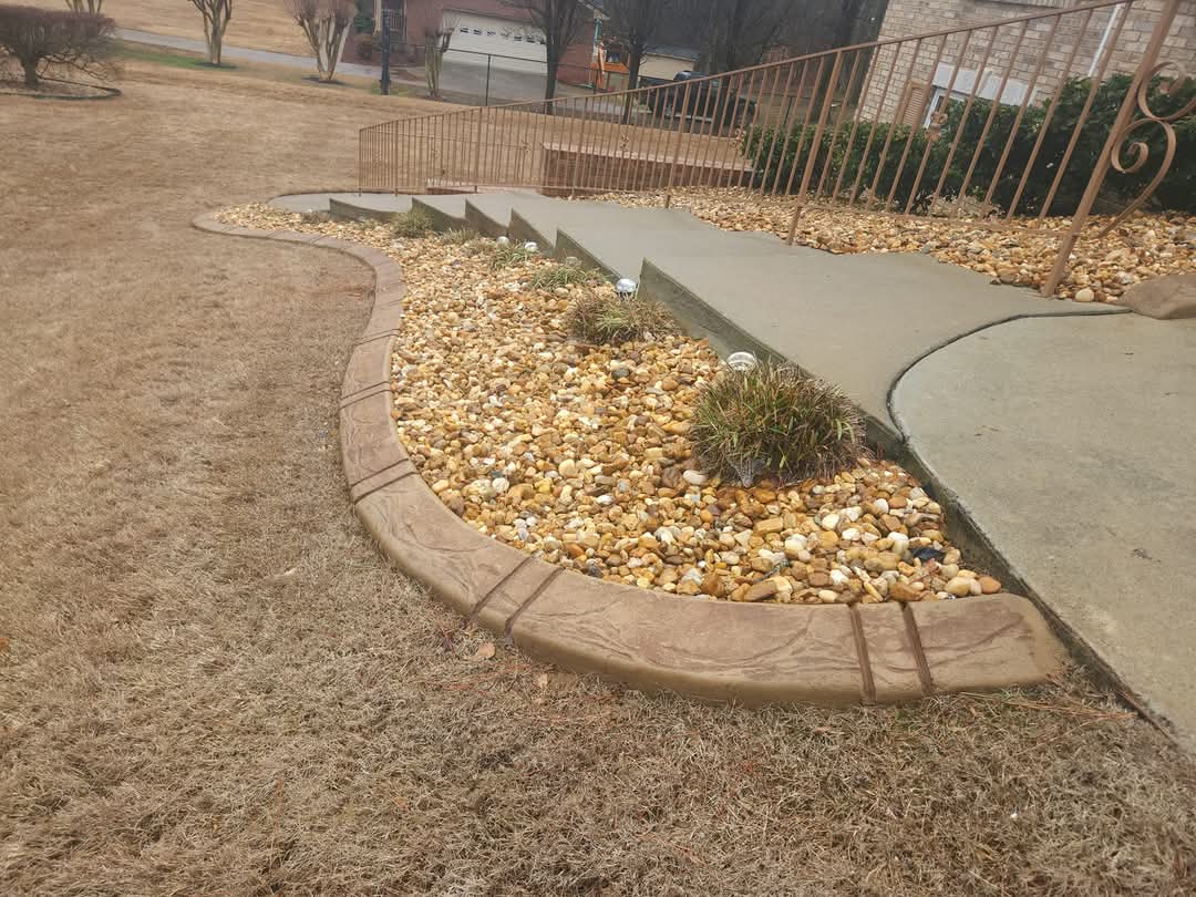 Long sweeping curved stamped concrete border along sloped yard with gold river rocks and landscape lighting