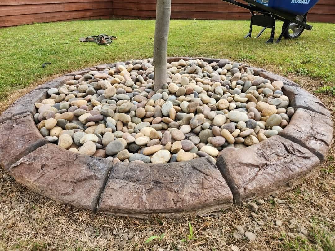 Natural stone stamped concrete tree ring filled with smooth river rocks surrounding mature tree trunk