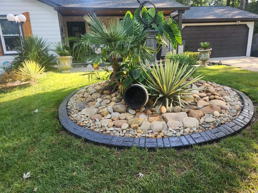 Circular dark slate stamped concrete curbing framing tropical rock garden with palm and elephant ear plants