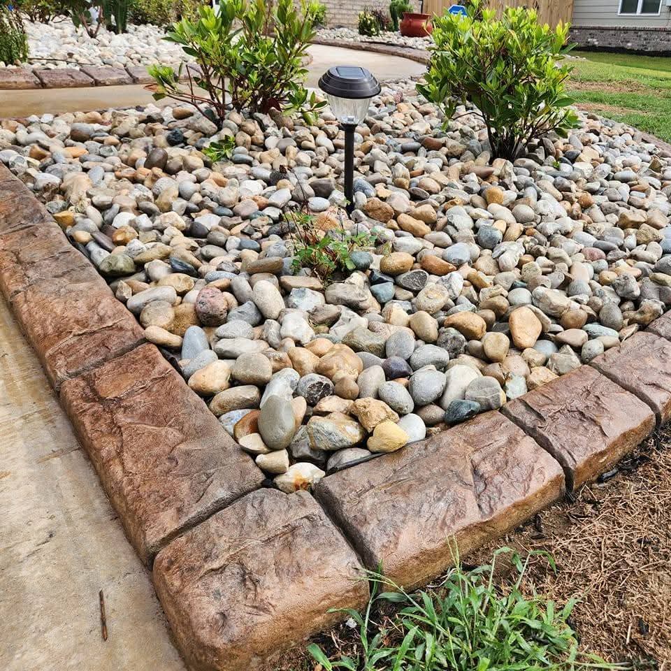 Warm brown stamped curbing bordering decorative river rock garden with solar light
