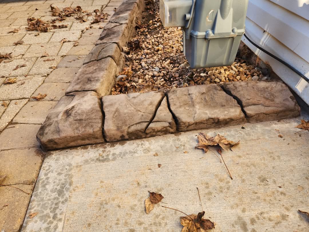Stamped concrete curbing edge along paver patio with decorative pebble bed and autumn leaves