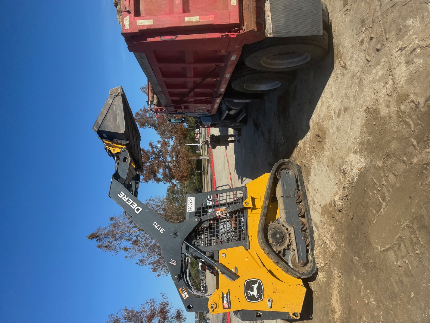 John Deere 317G skid steer loader alongside red dump truck ready for debris hauling