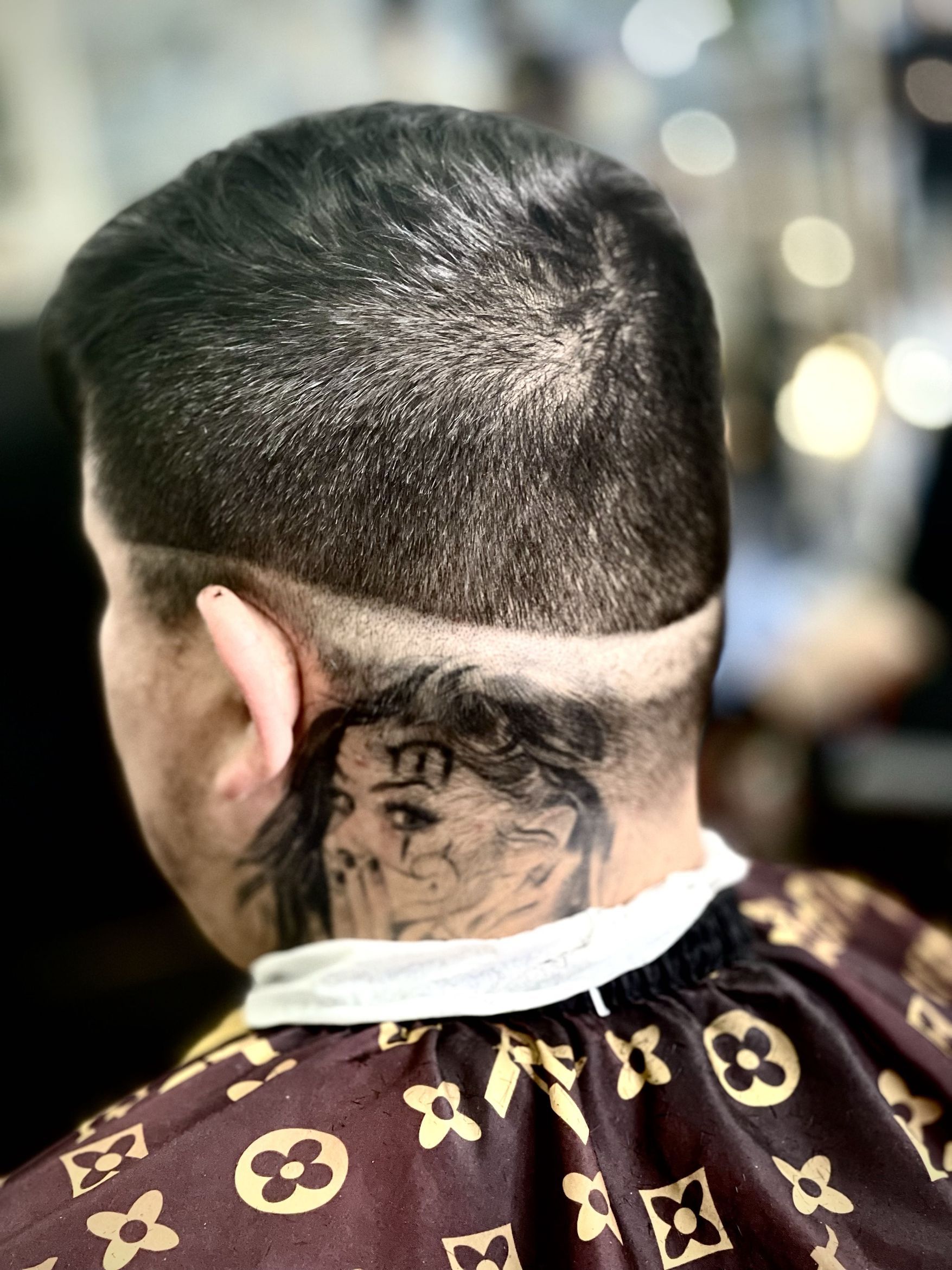 Back-of-head view showing a short textured crop with a detailed design line shaved into the nape area