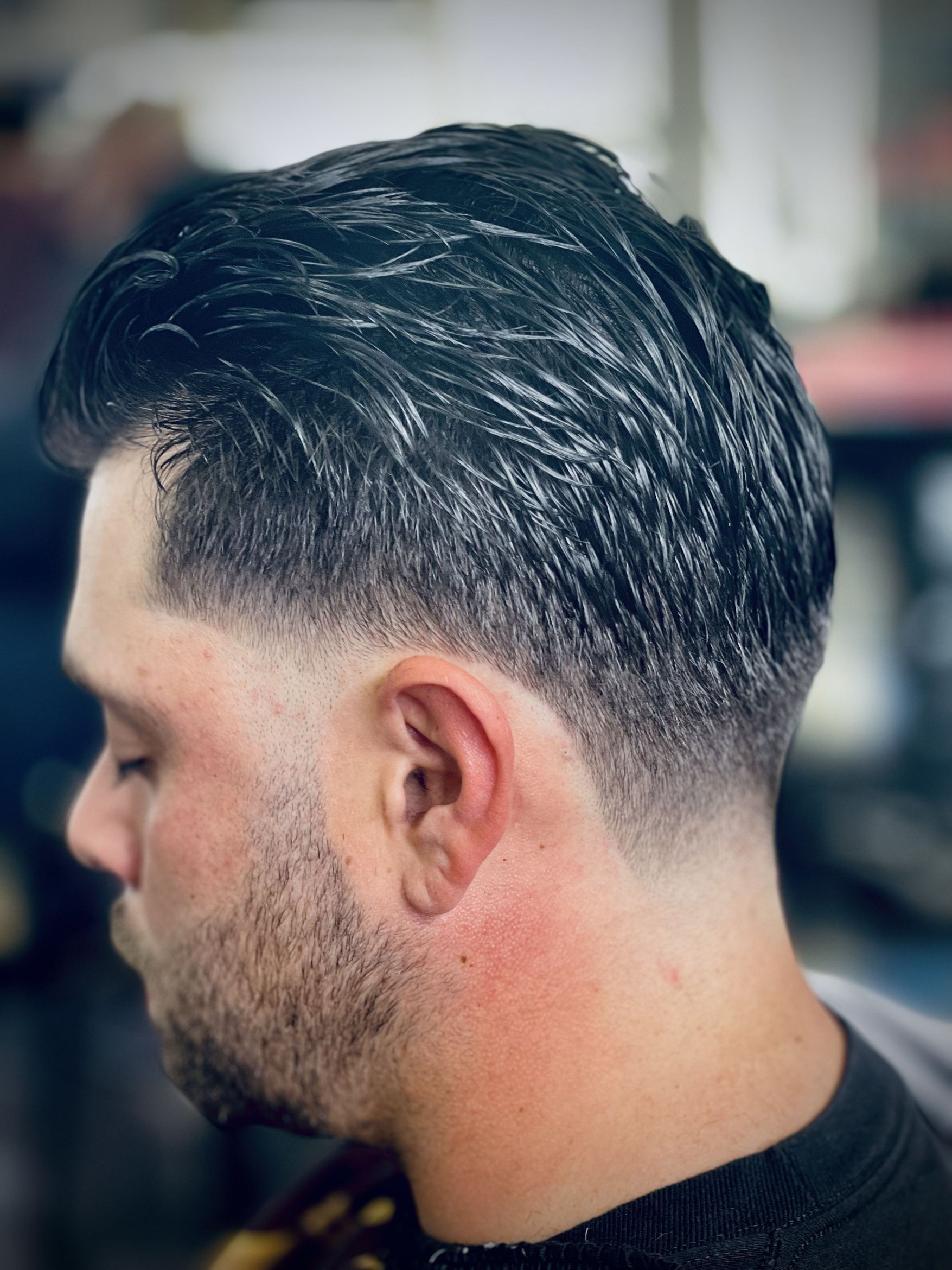 Rear three-quarter view of a low taper fade with textured wavy hair left longer on top