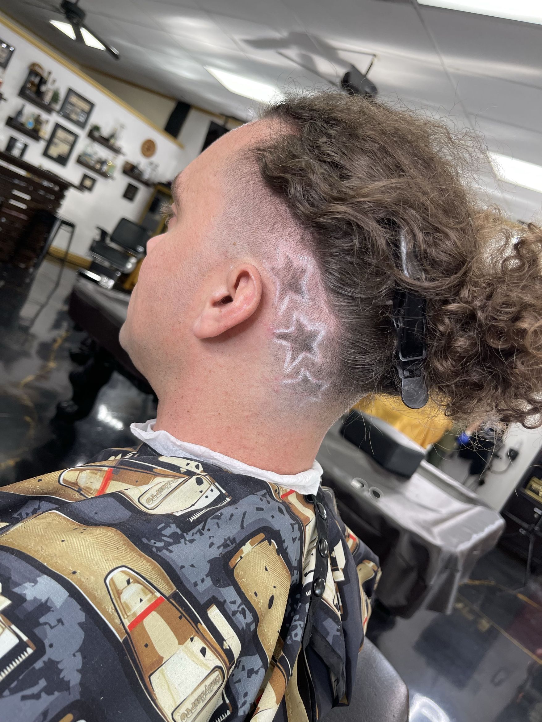 Side profile showing curly textured hair on top with a smooth skin fade and precise line work along the temple