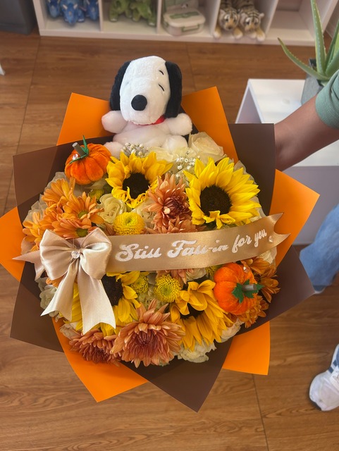 Autumn themed bouquet with plush Snoopy, sunflowers, warm orange chrysanthemums, white roses, mini pumpkins, and 'Still Fall-in for you' satin ribbon by FridAndre Florals