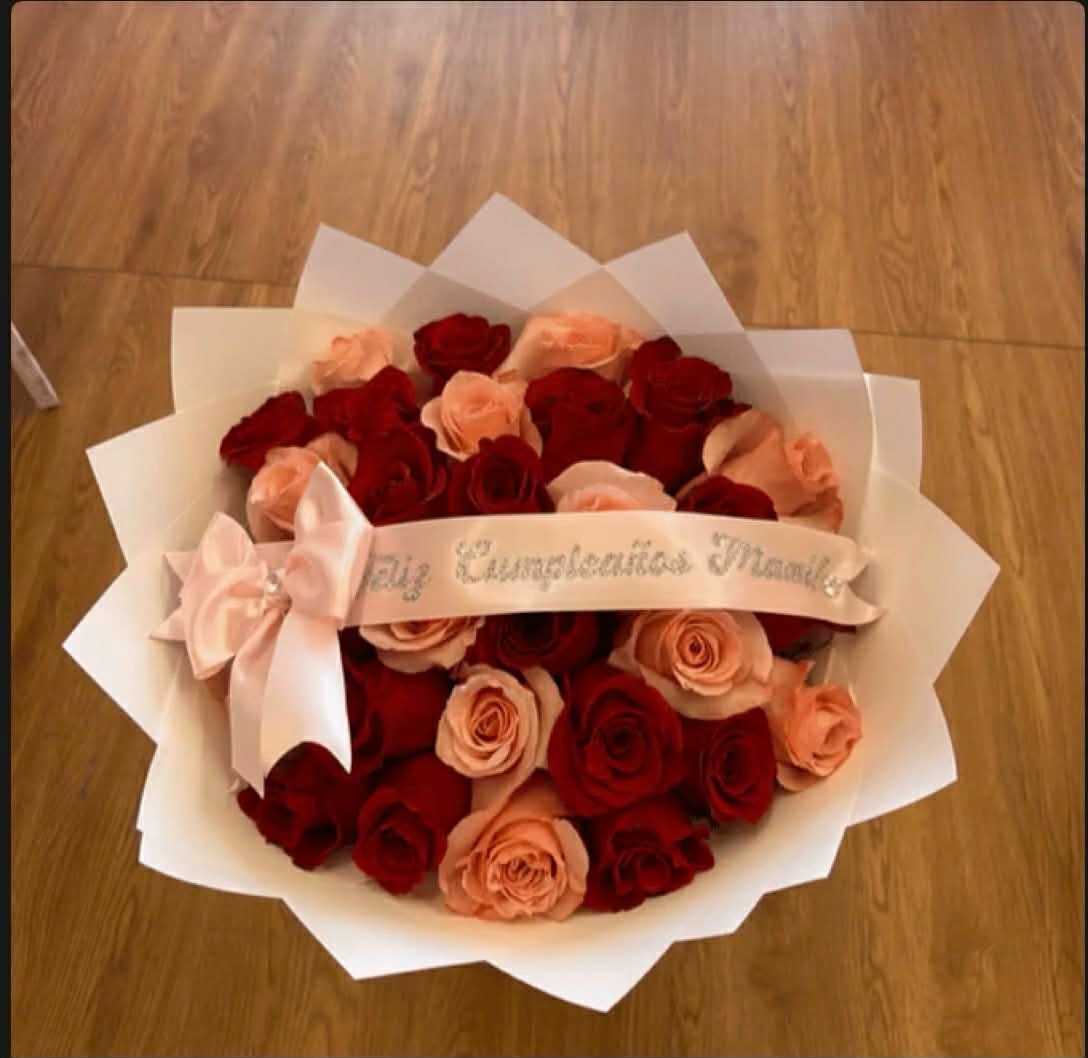Beautiful 'Feliz Cumpleaños Mamá!' red and peach pink Ecuadorian rose bouquet with 'Feliz Cumpleaños Mamá' gold-glitter lettered satin ribbon bow, elegant white geometric paper wrap, and large satin bow accent - birthday celebration arrangement for mom
