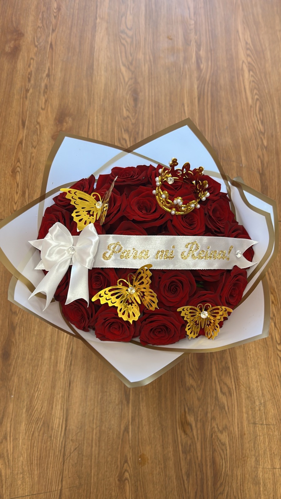 Romantic 'Para mi Reina!' 25-rose deep red Ecuadorian round rose bouquet with golden jeweled pearl crown tiara, three golden laser-cut butterfly decorations with crystal centers, 'Para mi Reina!' gold-glitter lettered white satin ribbon bow, and clean white geometric paper wrap - luxury romantic queen gift arrangement by FridAndre Florals