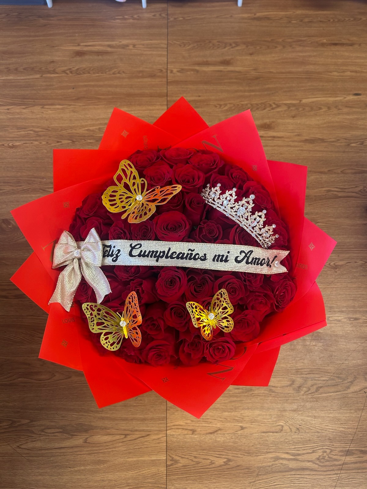 Stunning 'Feliz Cumpleaños mi Amor!' 50-rose deep red Ecuadorian rose round bouquet with sparkling crystal crown tiara, golden laser-cut butterfly decorations, gold satin bow, and vibrant red star-point paper wrap - luxury birthday love declaration arrangement by FridAndre Florals