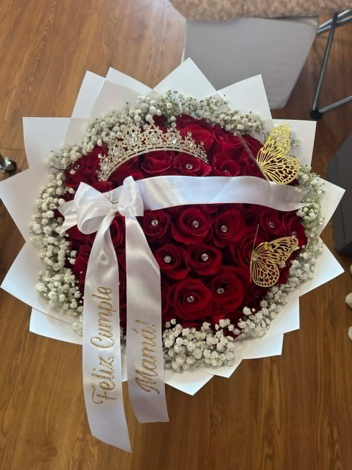 Stunning heart-shaped 50-rose deep red Ecuadorian rose bouquet with sparkling crystal crown tiara, golden laser-cut butterfly decorations, delicate white baby's breath border, 'Feliz Cumpleaños' and 'Mi Amor' gold-glitter lettered white satin ribbon bows, and elegant white geometric paper wrap - luxury birthday love declaration arrangement by FridAndre Florals