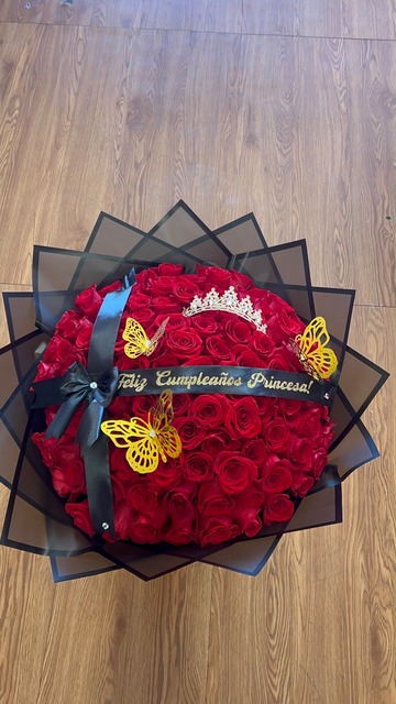 Stunning '¡Feliz Cumpleaños Princesa!' 100-rose red Ecuadorian round bouquet with sparkling crystal crown tiara, golden laser-cut butterfly decorations, black satin ribbon with gold script, and black star-point wrap by FridAndre Florals
